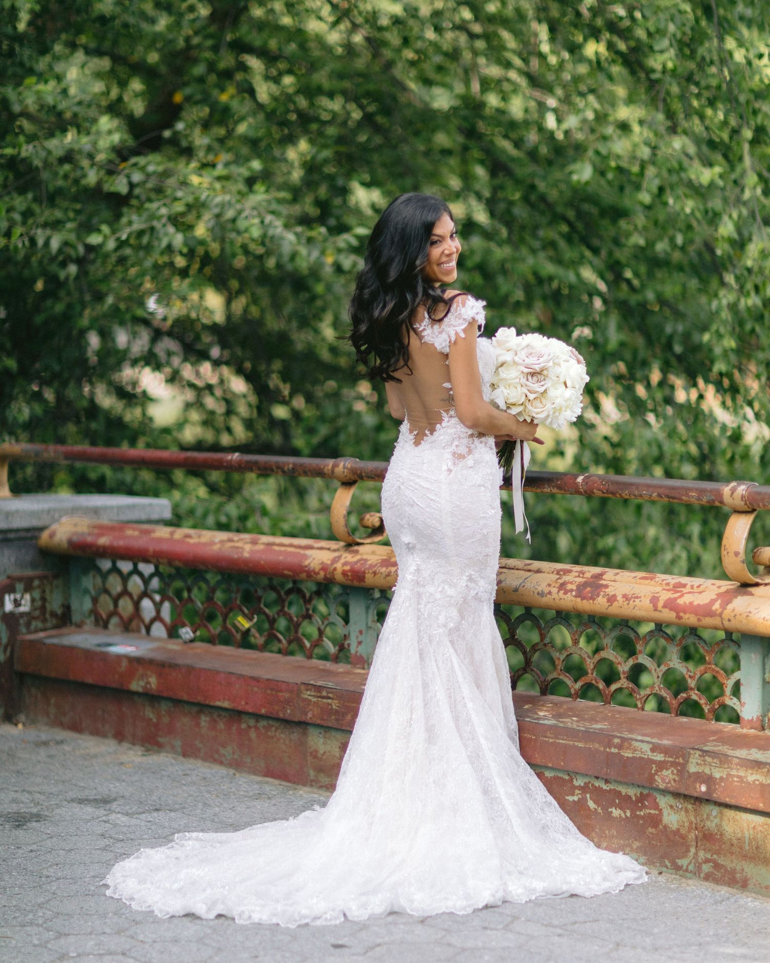 Elegant lace mermaid wedding dress with long train shown in outdoor bridal portrait.