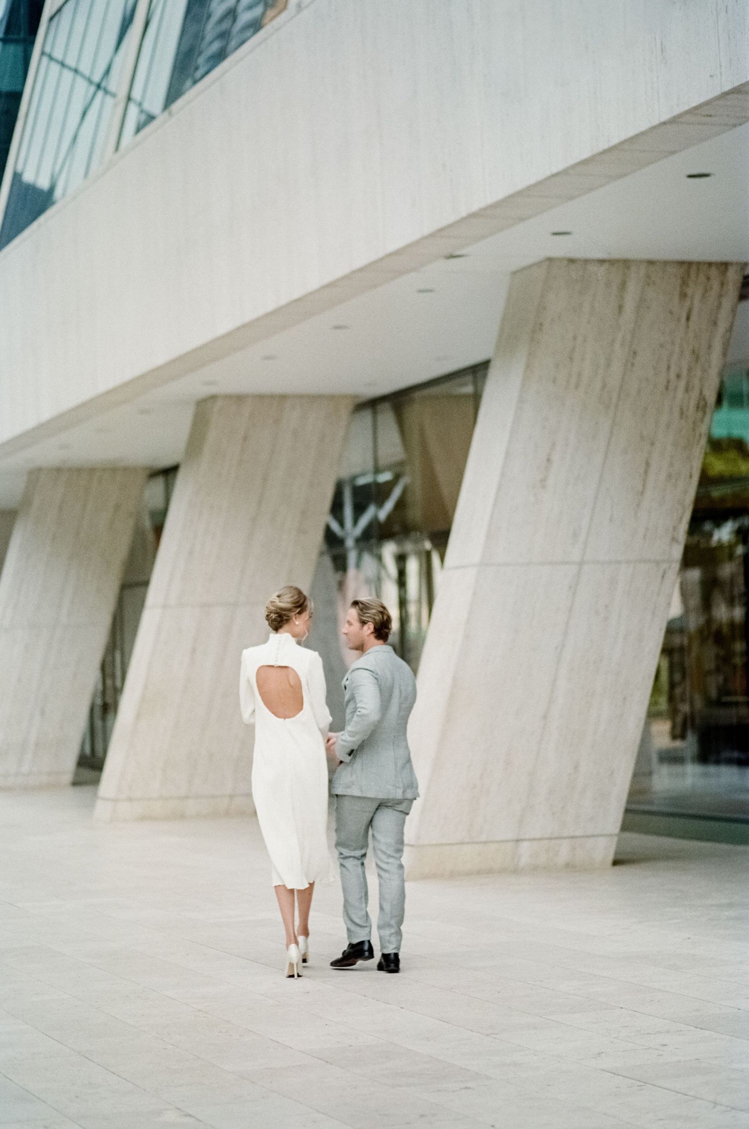 Couple in formal wear walking together near modern architectural columns.