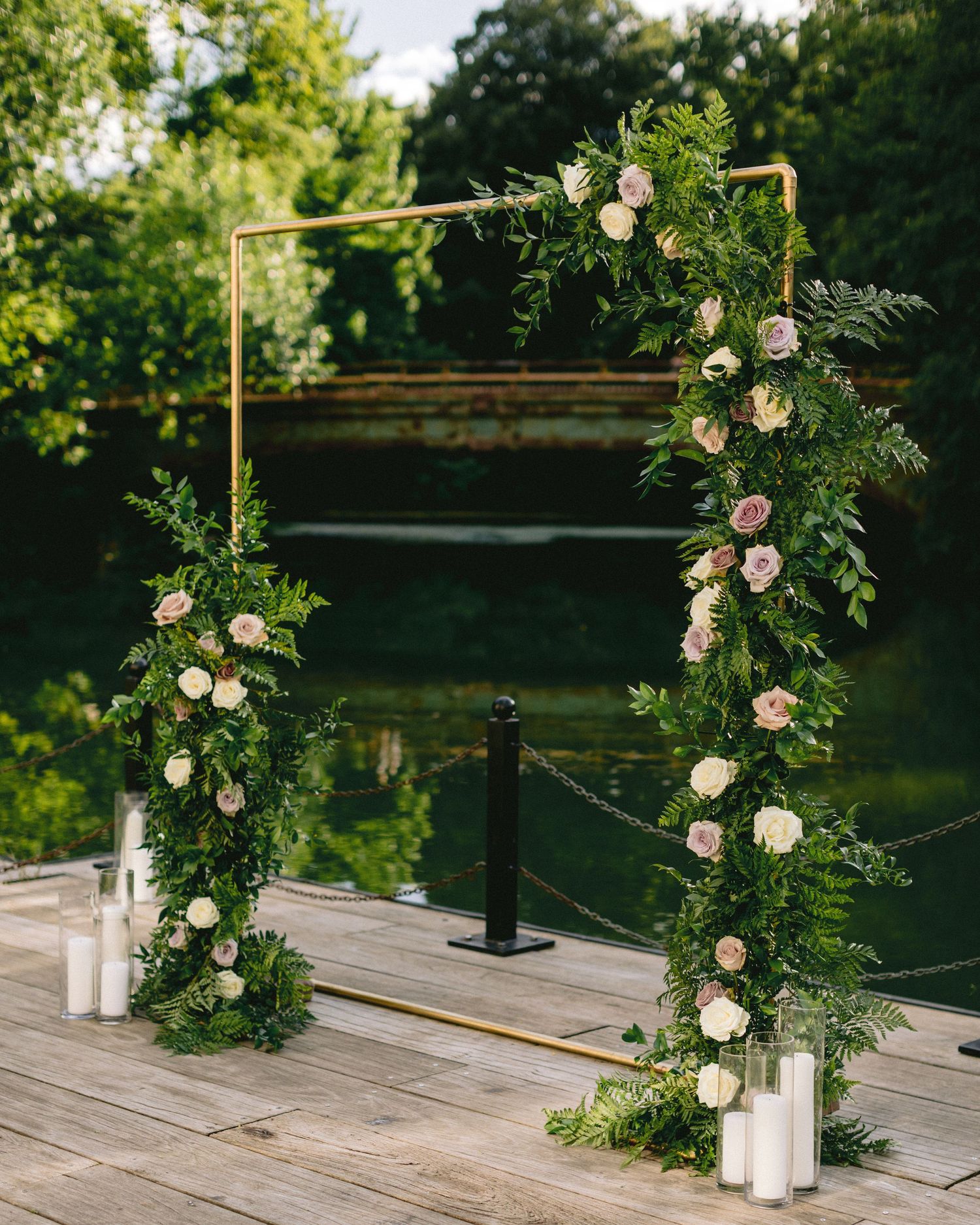 A minimalist wedding arch with white roses and greenery against a natural outdoor backdrop.