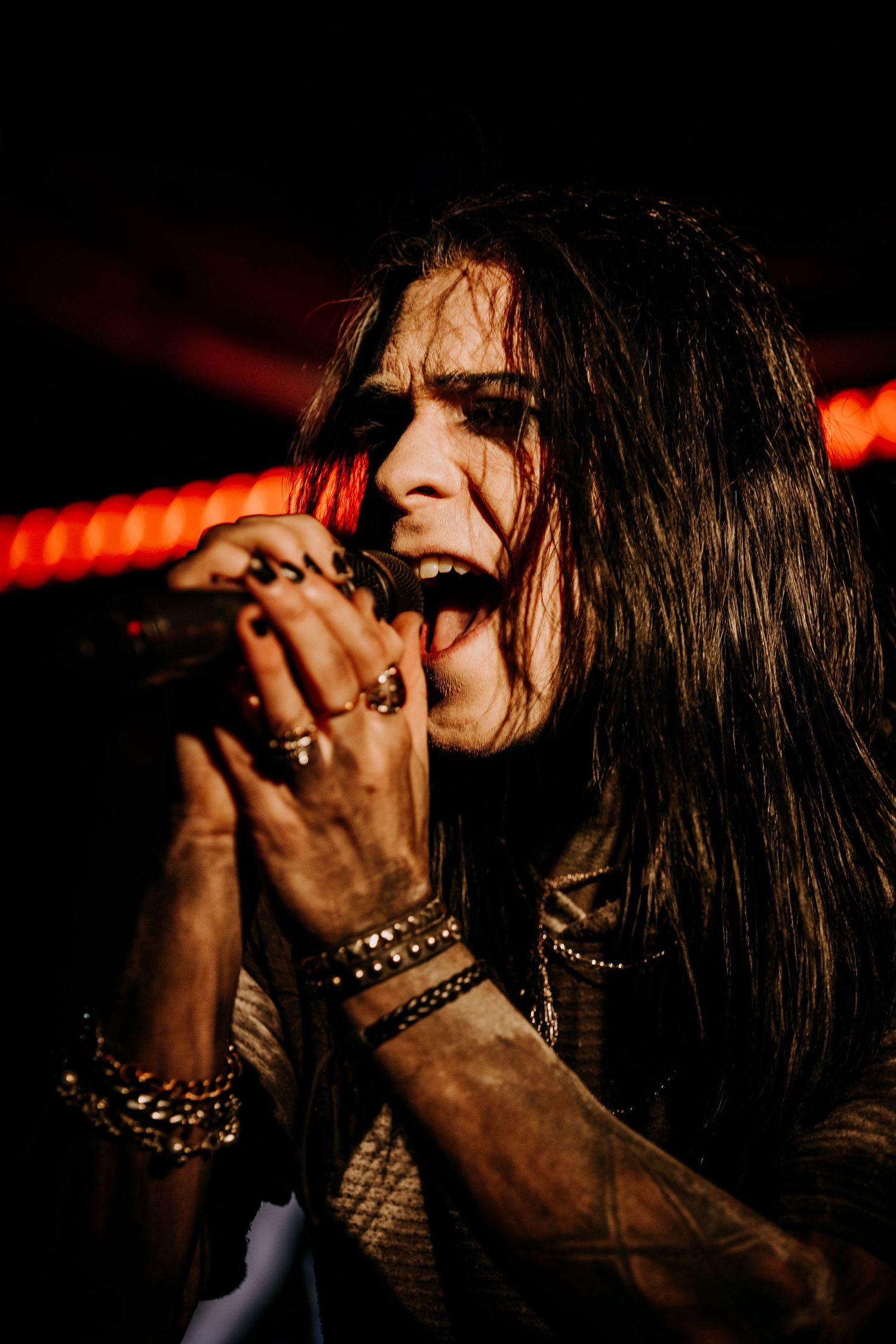 Concert vocalist sings passionately into microphone wearing multiple bracelets.