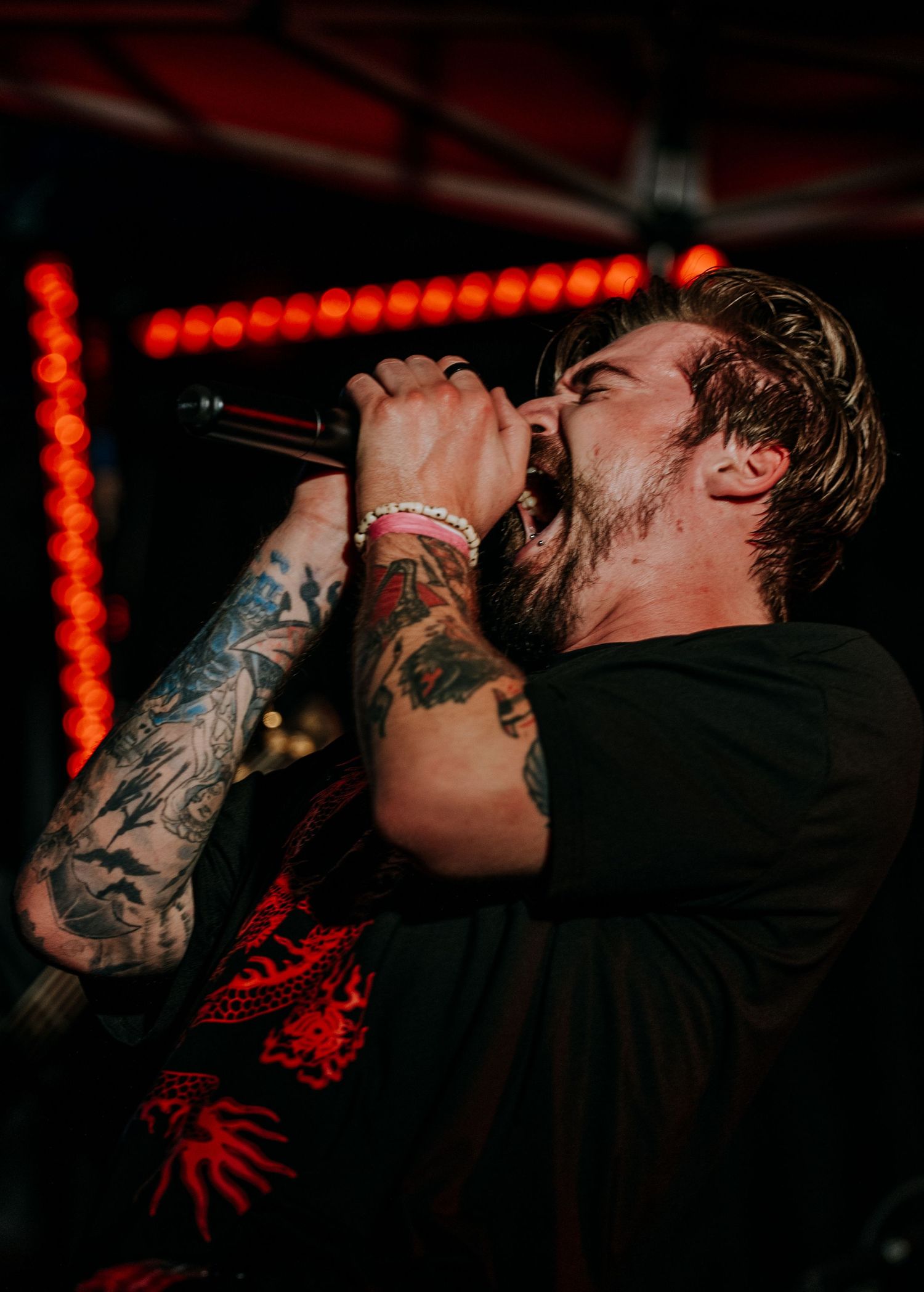 Metal singer performs passionately with microphone at concert with red lighting in background.