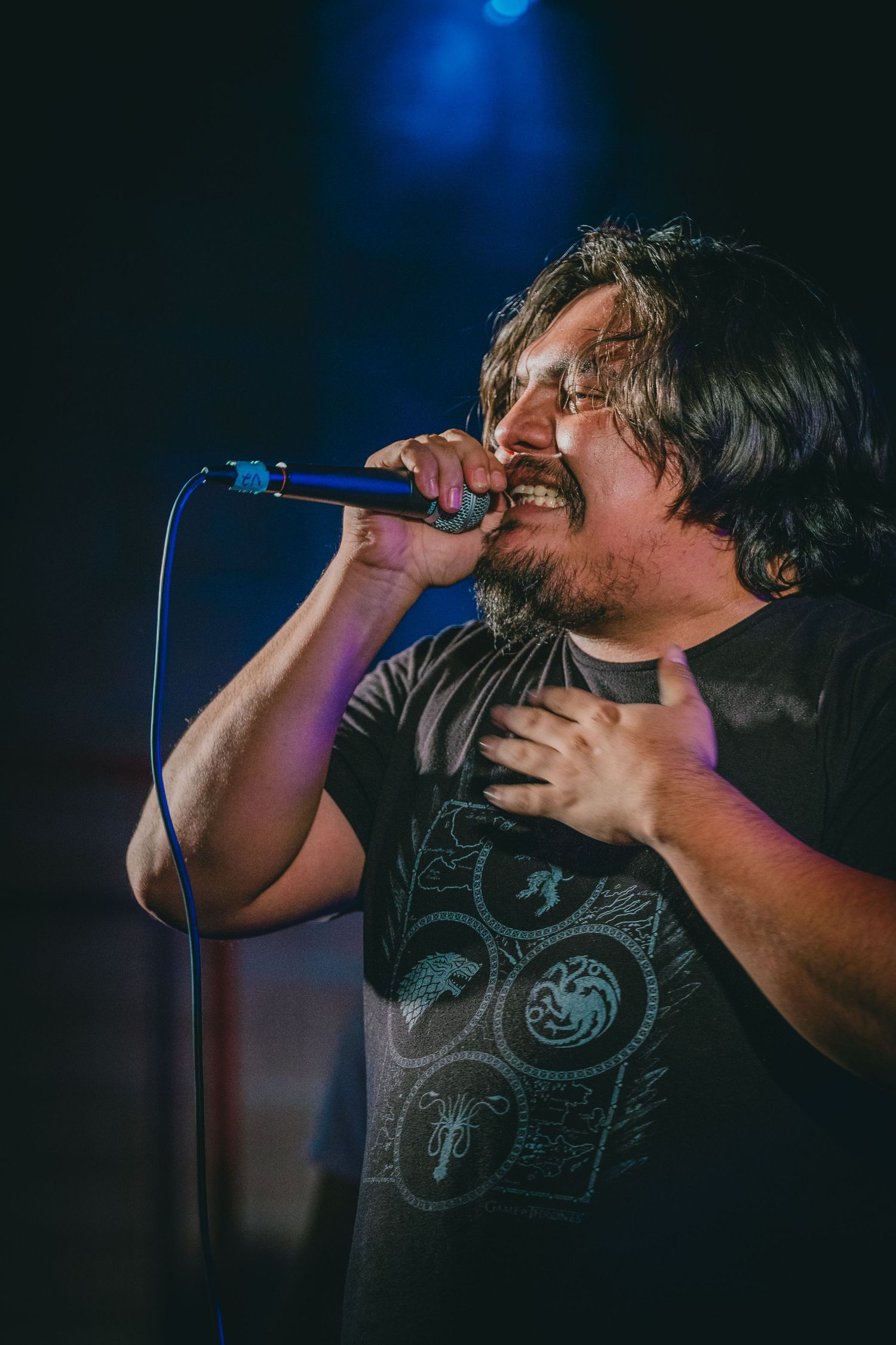Passionate vocalist singing into microphone during live performance with blue stage lighting.