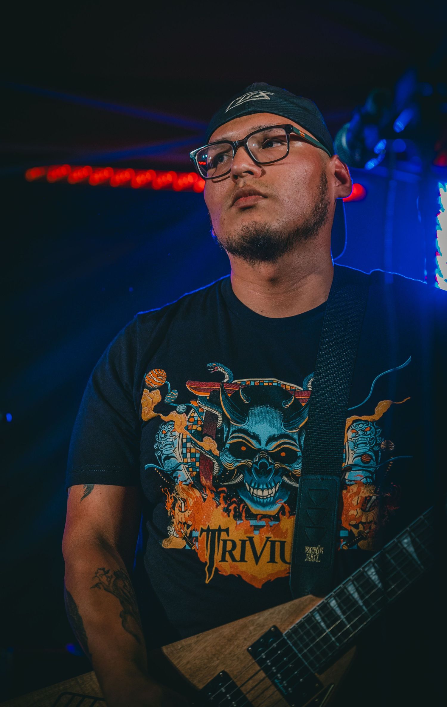 Guitarist in baseball cap and skull t-shirt performing under stage lights.