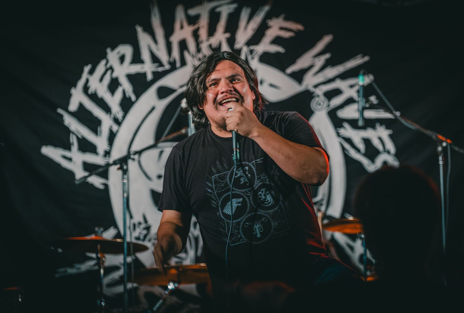 Energetic rock singer performs in front of Alternative Music logo backdrop.