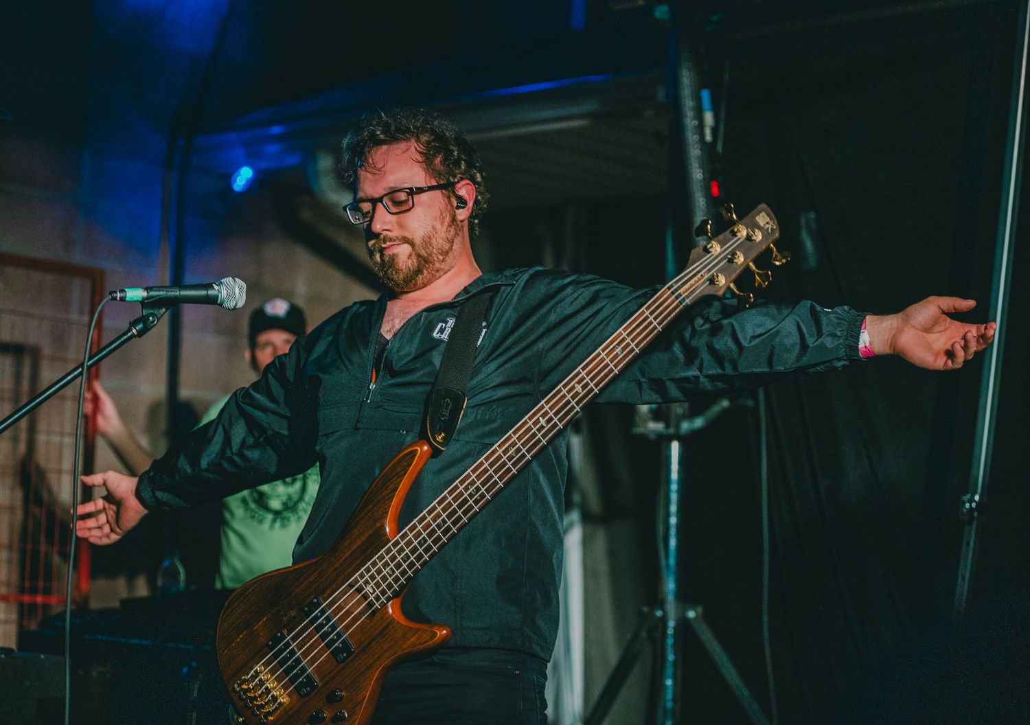 Bass guitarist performing with expressive stance under blue stage lighting.