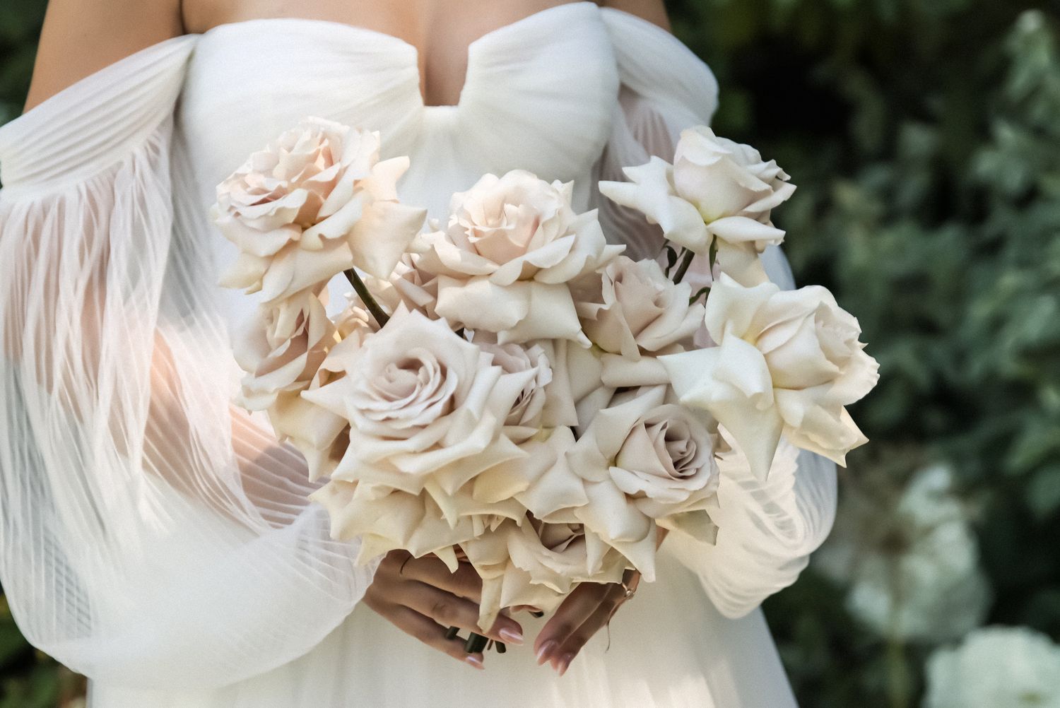Cora Emilie Media Close-up of elegant white rose and gardenia wedding bouquet against natural background.