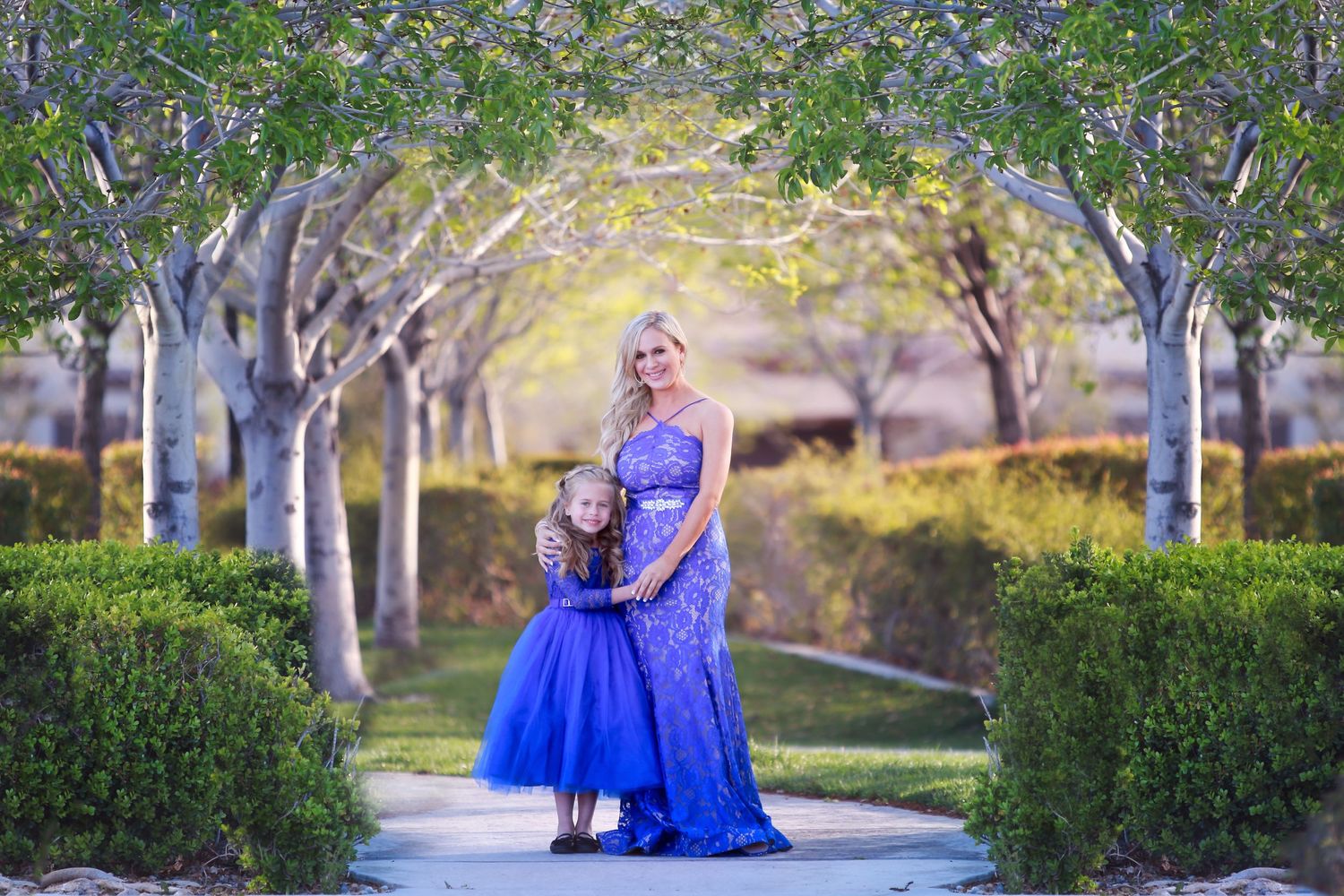 Elegant outdoor photo session with flowing blue gowns in a tree-lined path.