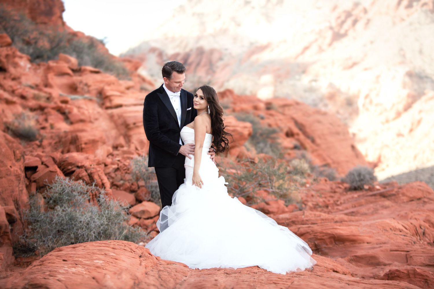 Newlyweds share intimate moments against a backdrop of dramatic red rock cliffs.