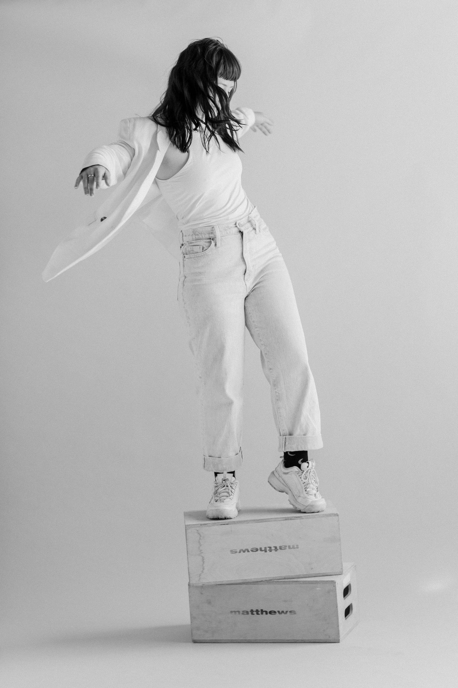 Black and white photo of a person dancing on boxes wearing white clothing and sneakers.
