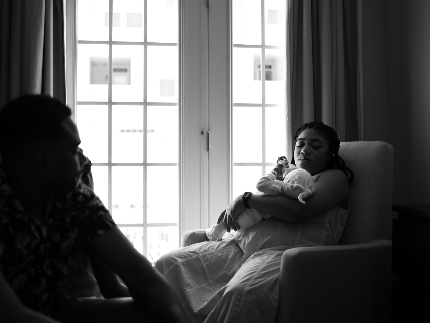 Woman Bottle-feeding Newborn Baby In A Chair In Front Of A Window