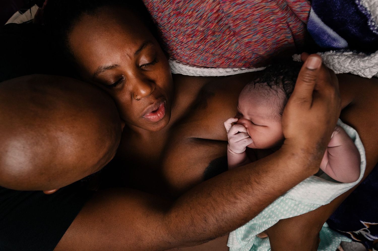 Black Family Embrace After Home Birth While Mother Holds Newborn And Father Holding Baby's Head