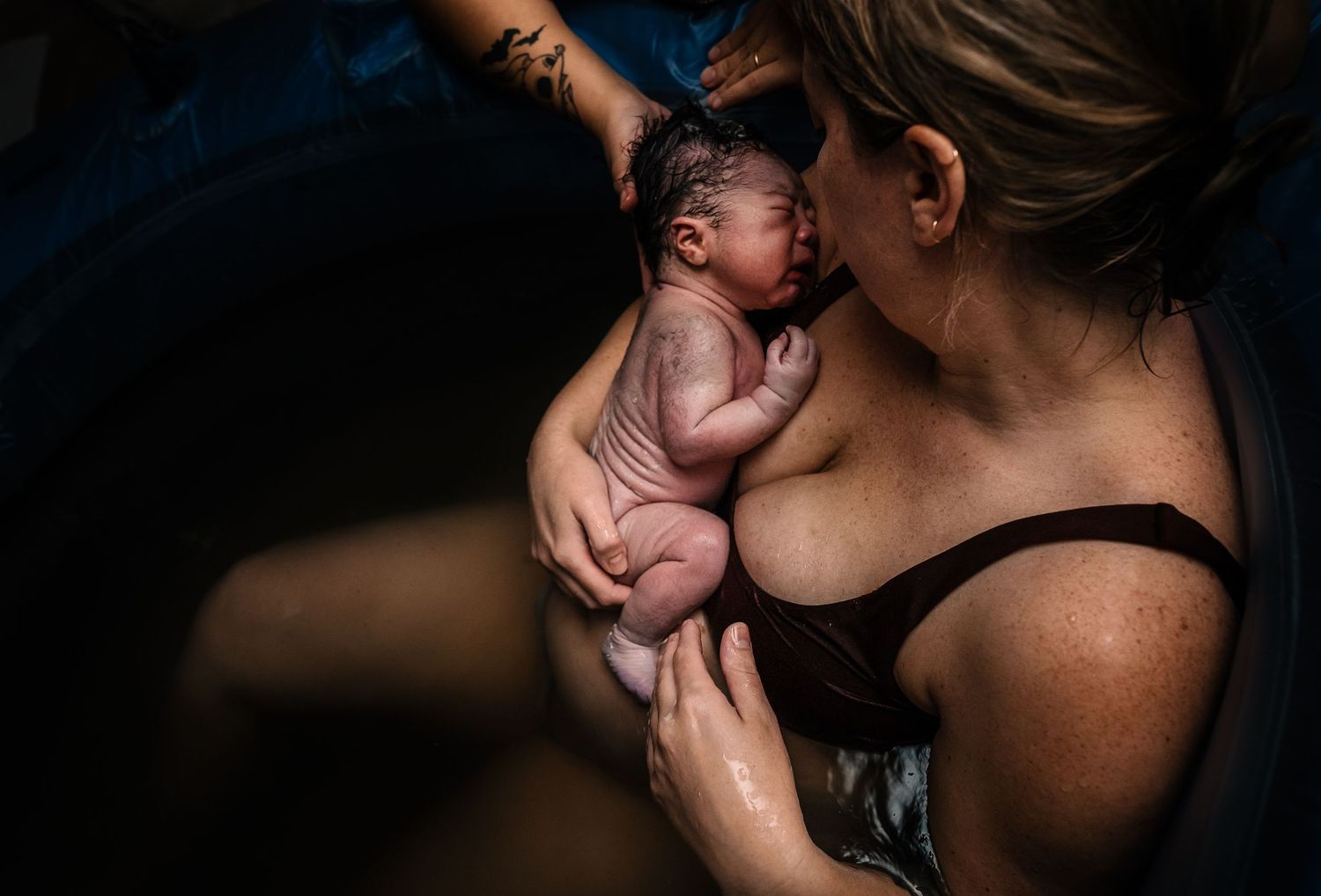 Woman sitting in water holding newborn baby and looking at wrinkled newborn baby