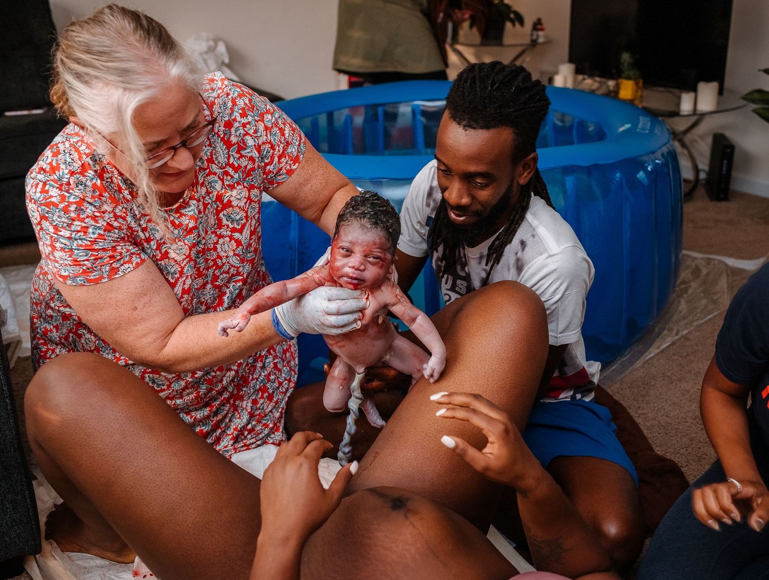 Woman Giving Birth With Midwife And Father Holds Baby Up With Umbilical Cord Attached