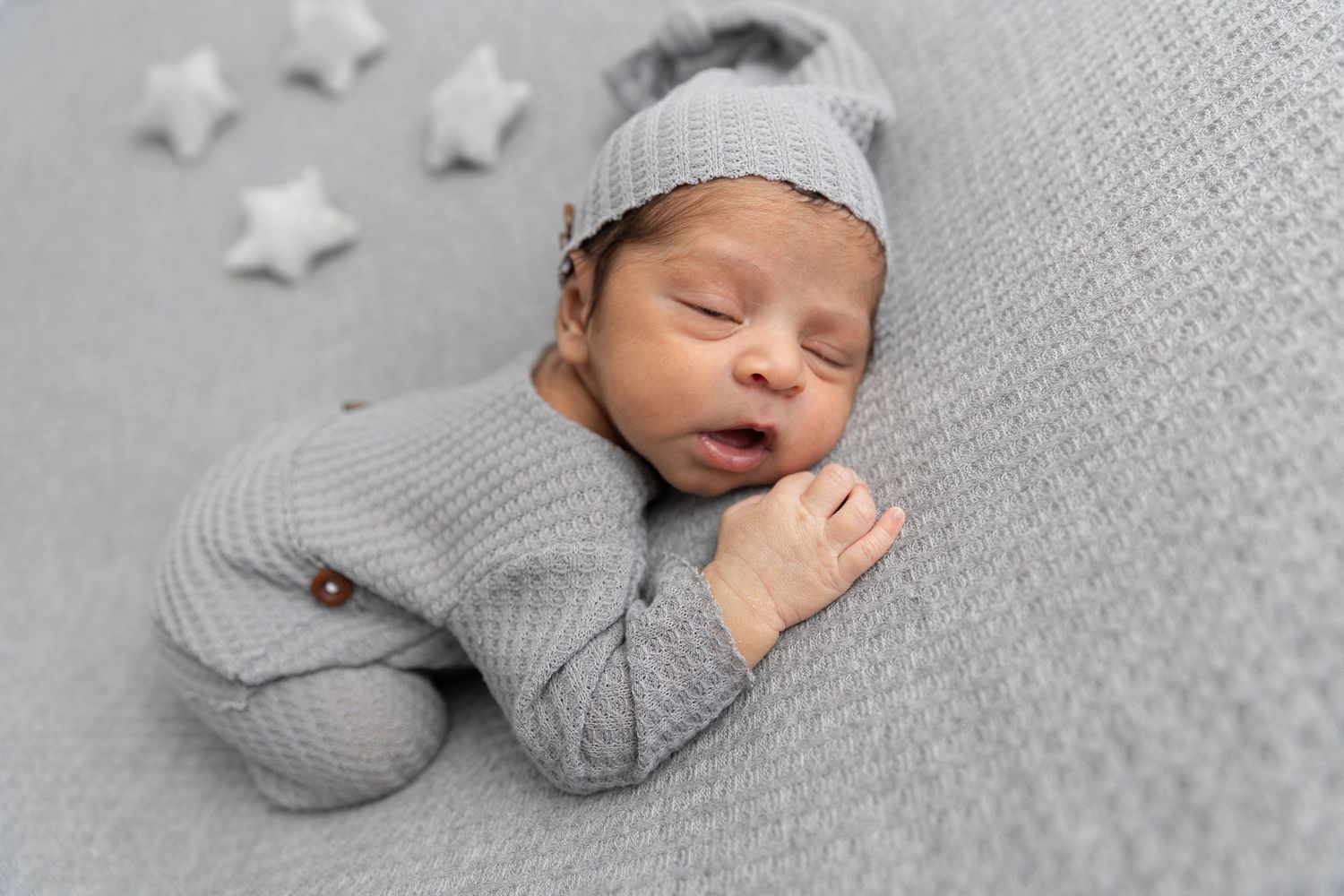 A sleeping baby in gray knit outfit lies on textured gray fabric with decorative stars.