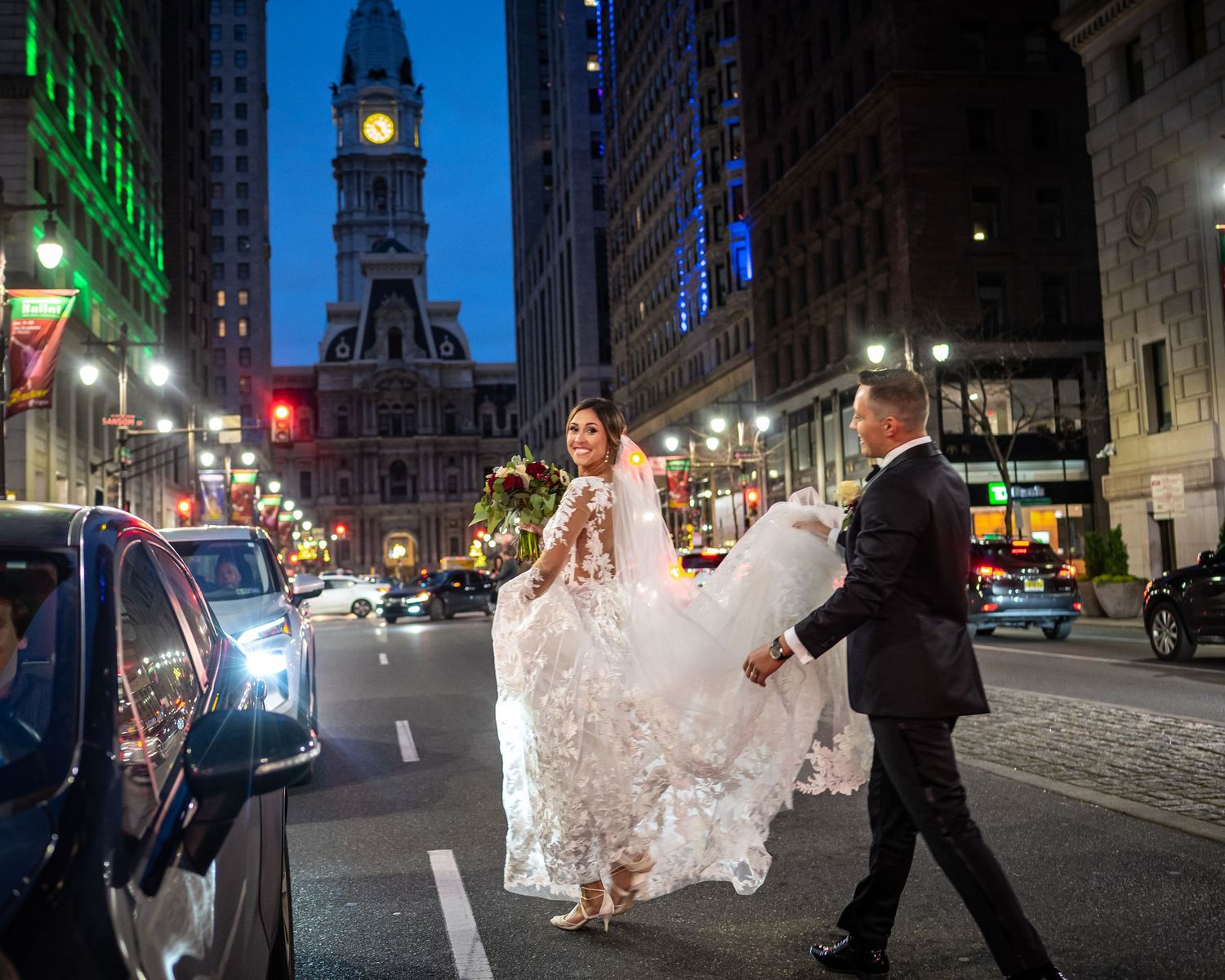 A bride in a flowing white dress poses on a city street with Philadelphia City Hall in the background.