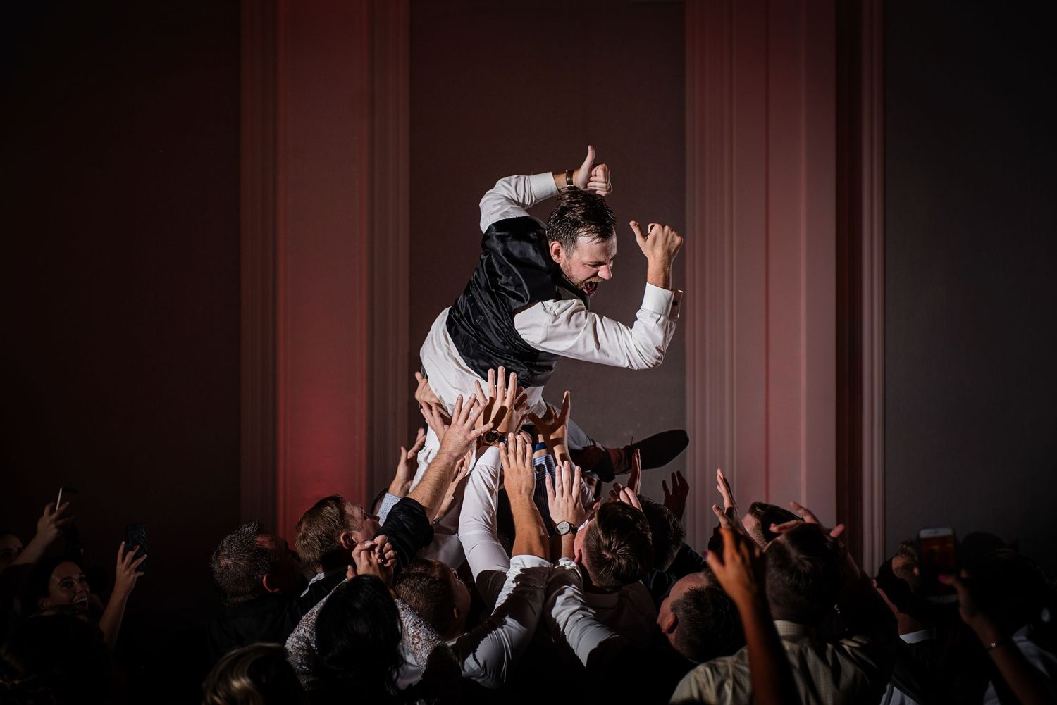 A crowd surfer is lifted above an energetic concert audience in dramatic lighting.