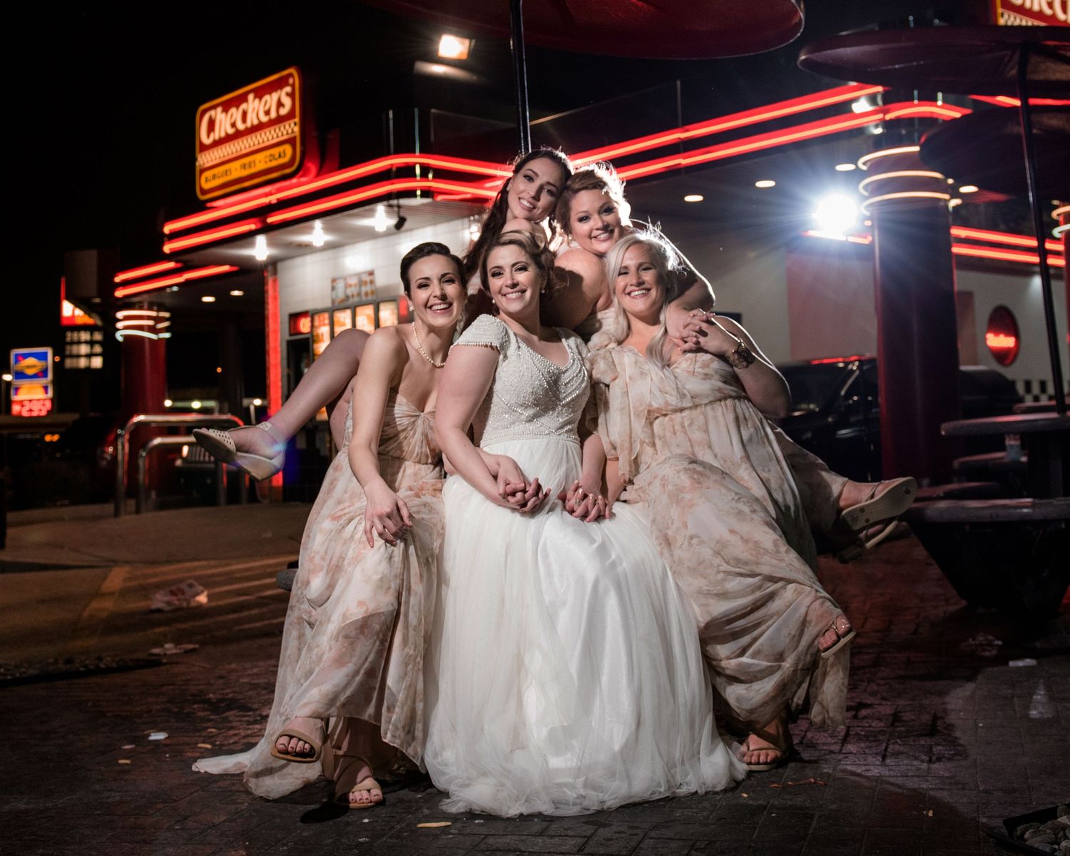 A wedding party poses for a fun nighttime photo outside a diner with neon signs.