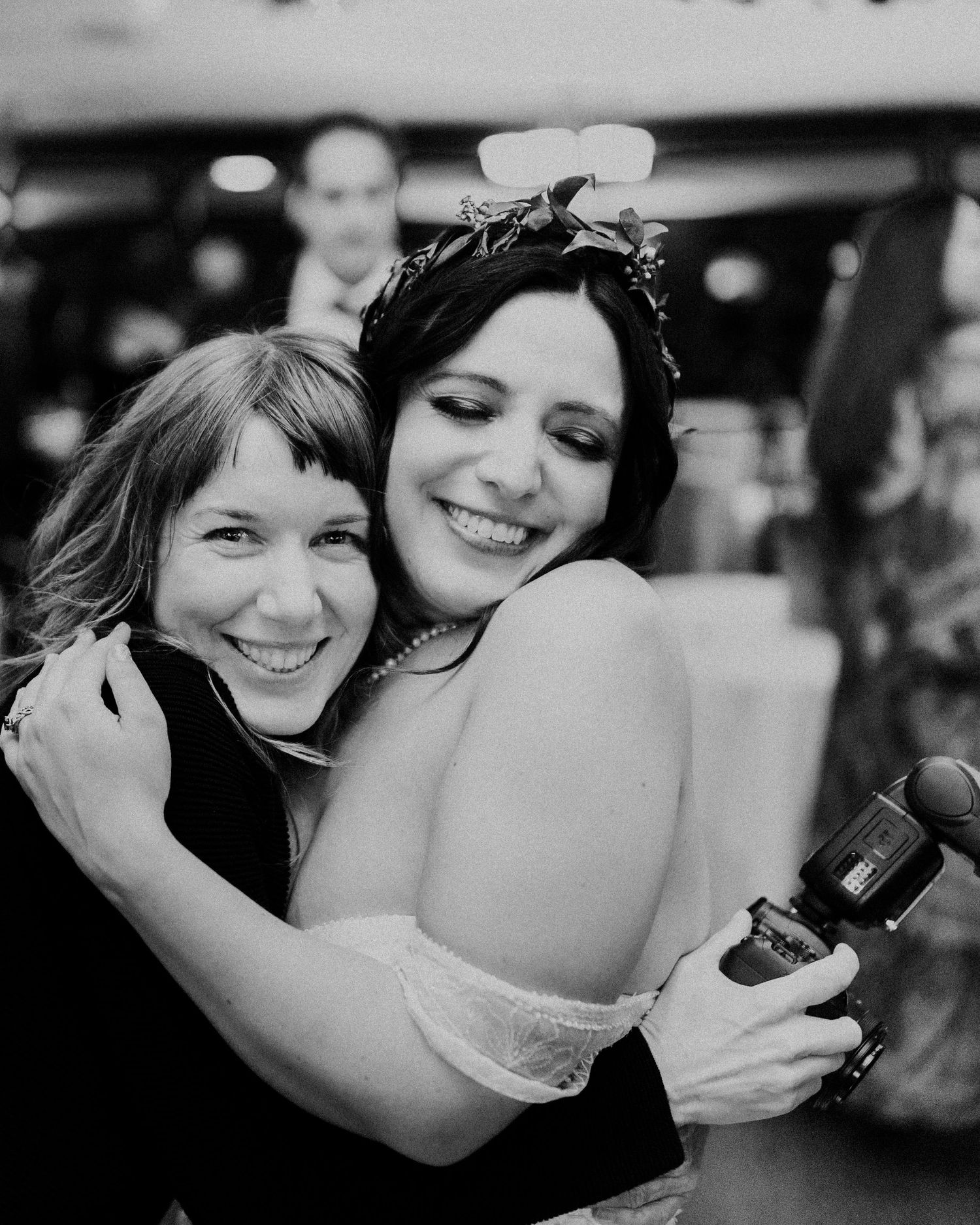 Two people sharing a joyful embrace while holding a camera at a celebration.