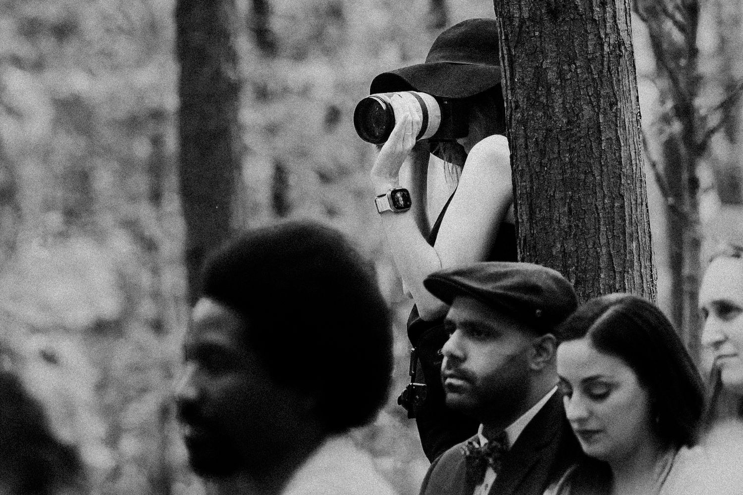 Photographer with telephoto lens taking photos from behind a tree in black and white.