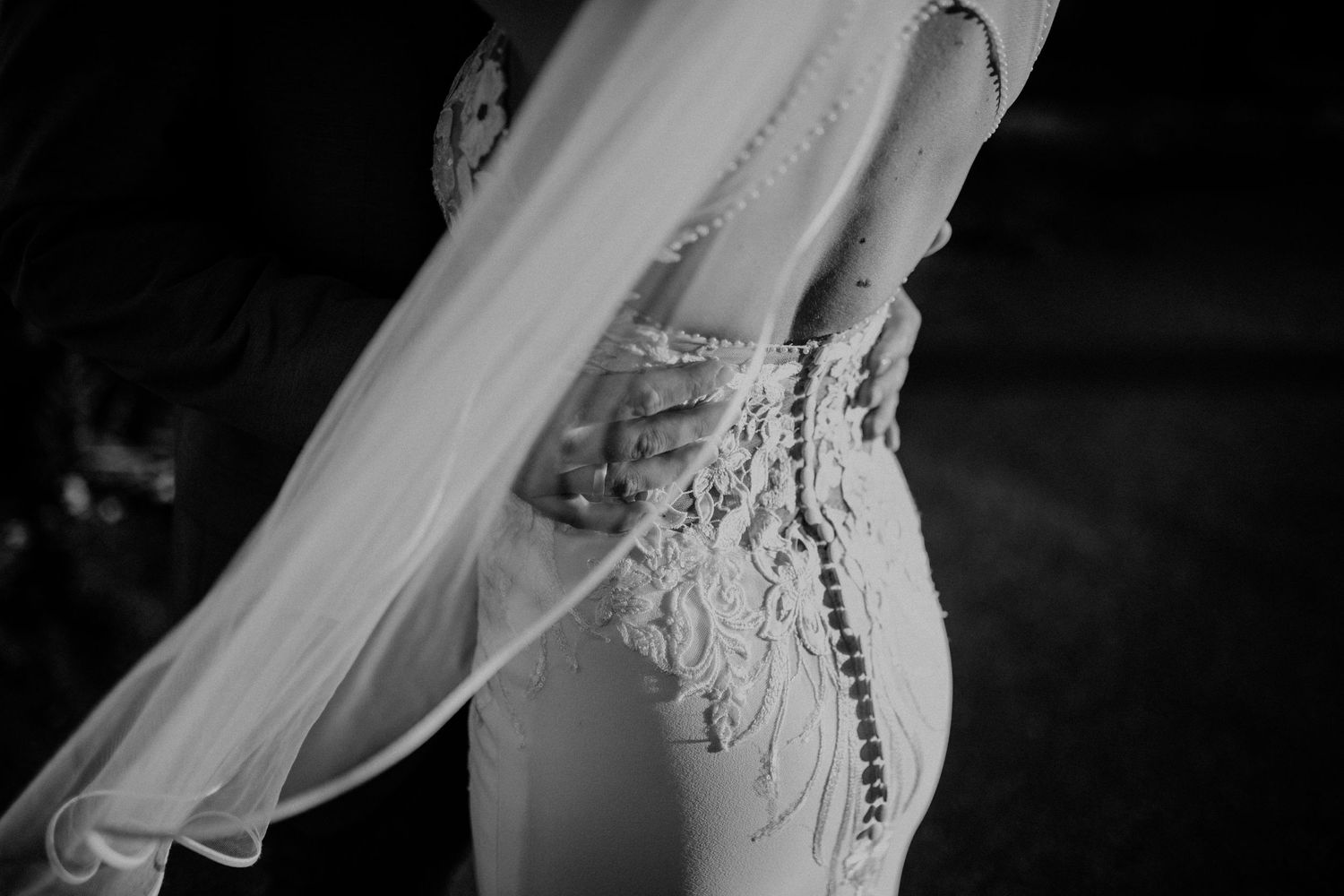 Close-up of a bride in a fitted lace wedding dress with intricate beading, black and white photo.