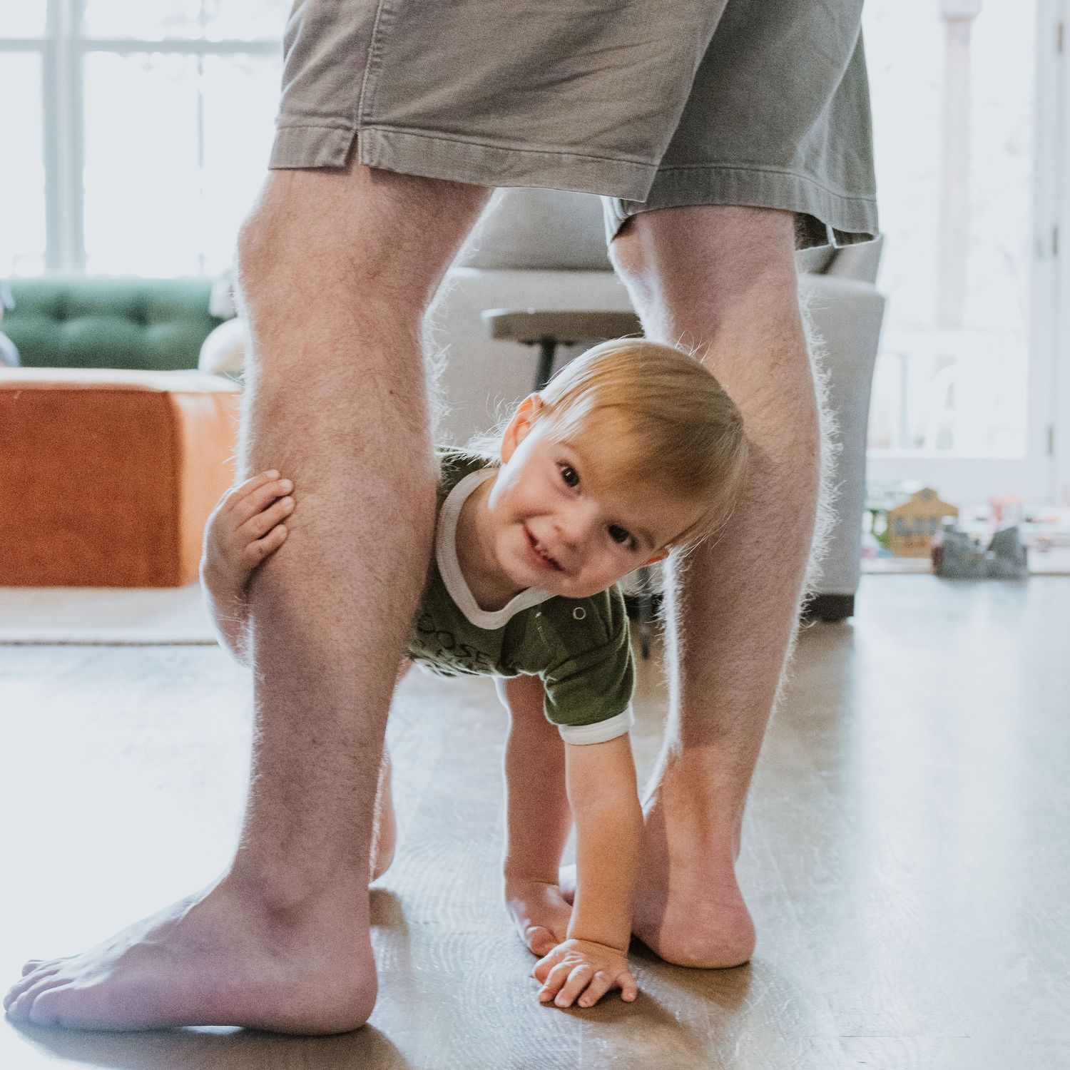 toddler looking at camera through dad's legs