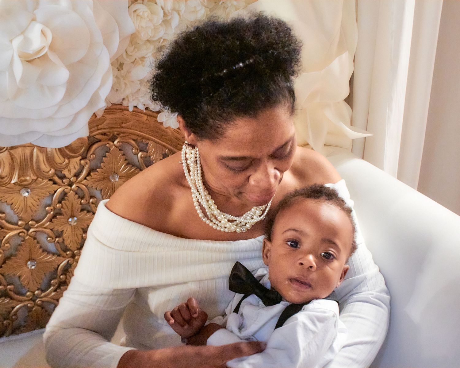 A tender family moment of parent and child in formal attire resting on an elegant vintage chair.