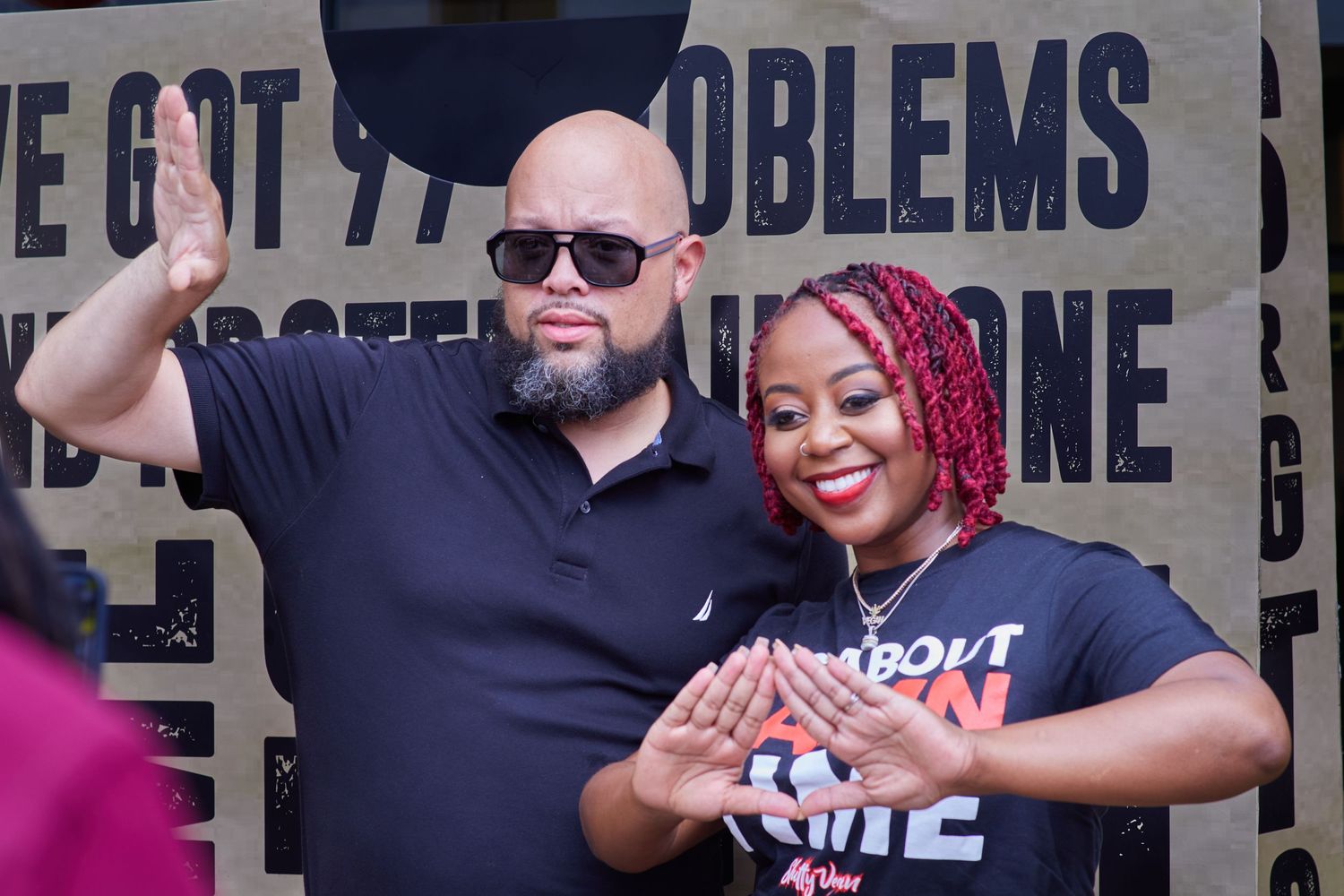 Two people posing against wall with motivational text at community event.