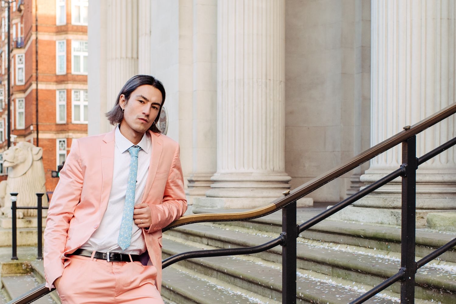 A person in a pink blazer poses against a column in different positions for a stylish photo series.