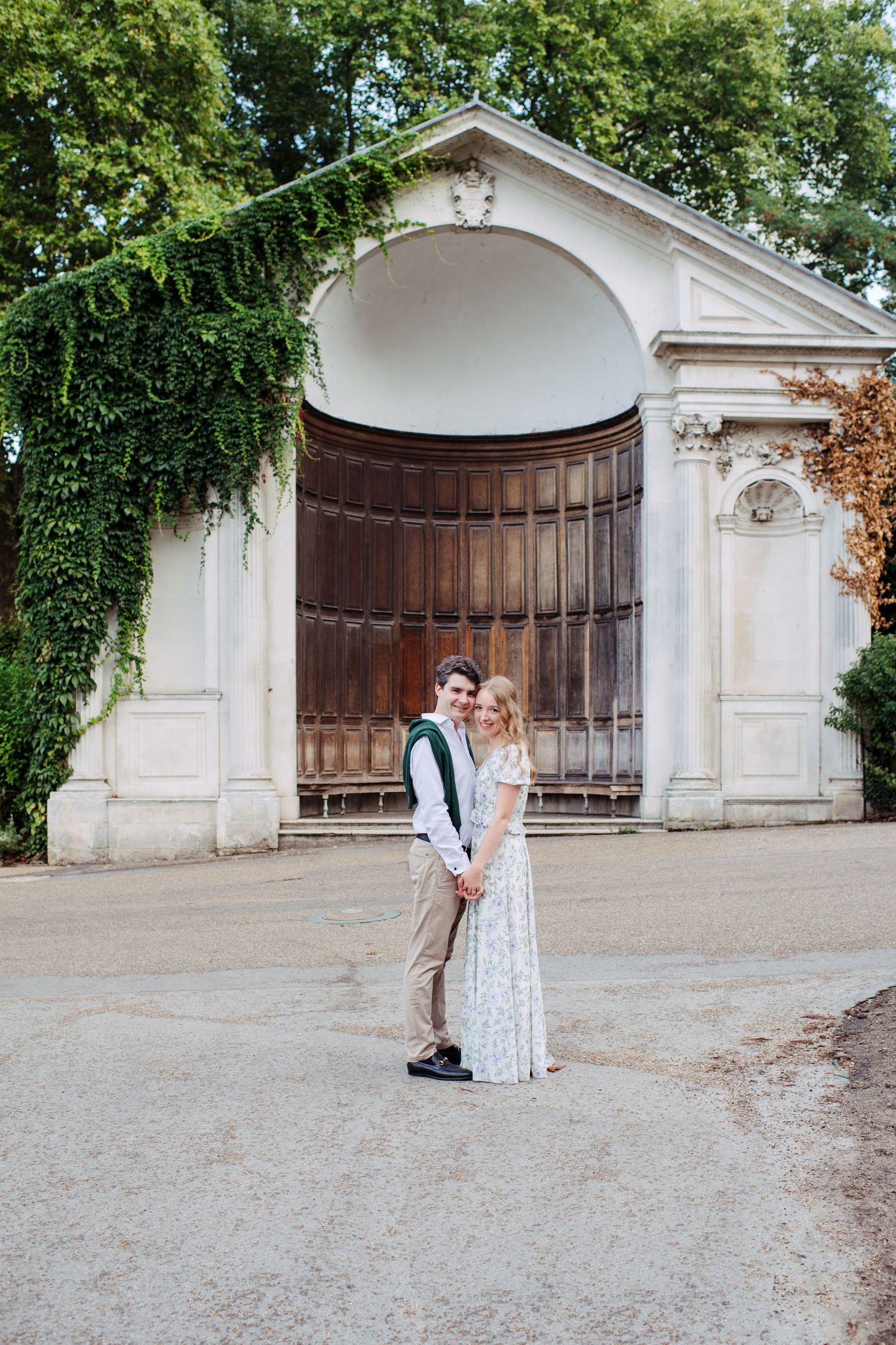 A romantic photo taken against a grand archway entrance with wooden doors and climbing vines at a historic venue.