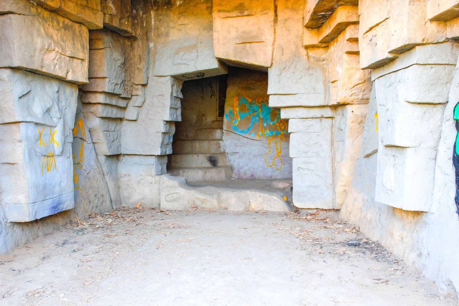 Ancient stone cave entrance with weathered rock formations and faded graffiti on the walls.