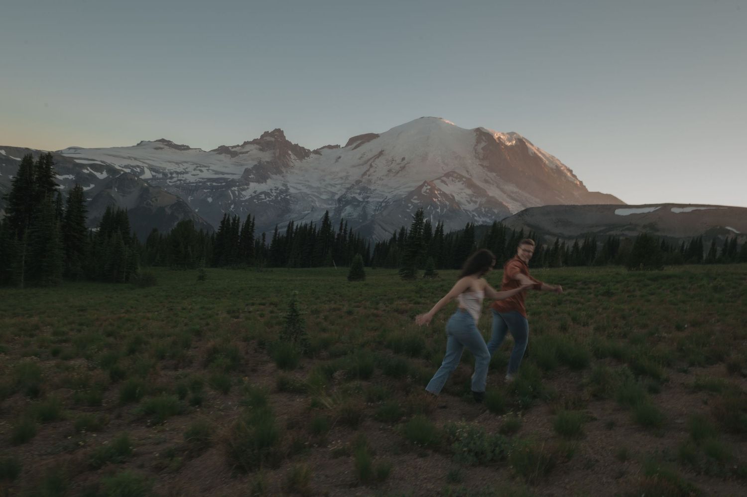 A playful couple dances in a meadow with Mount Rainier rising majestically in the background.