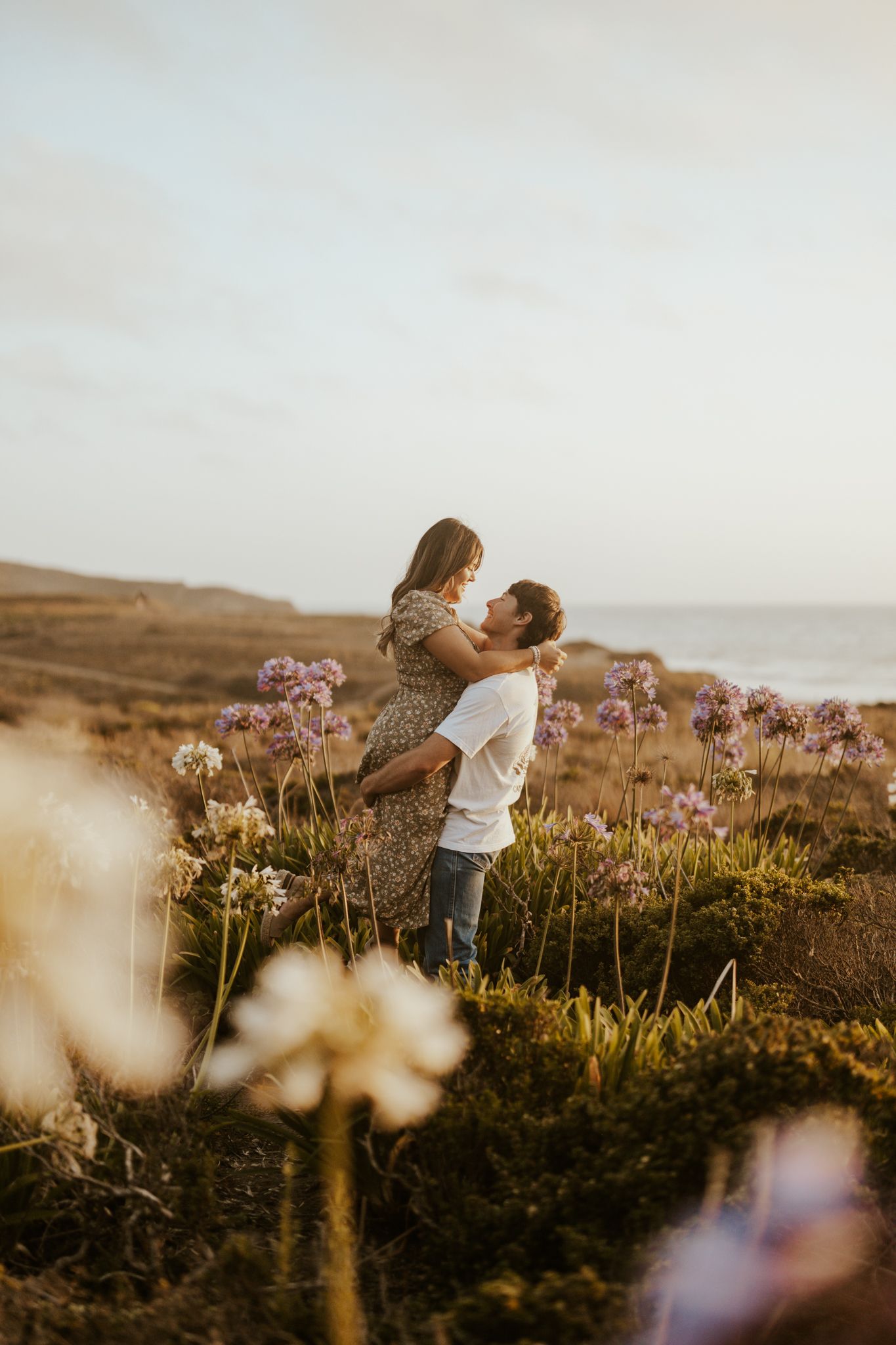 couple in the middle of a flower field, man is lifting woman up, sunset