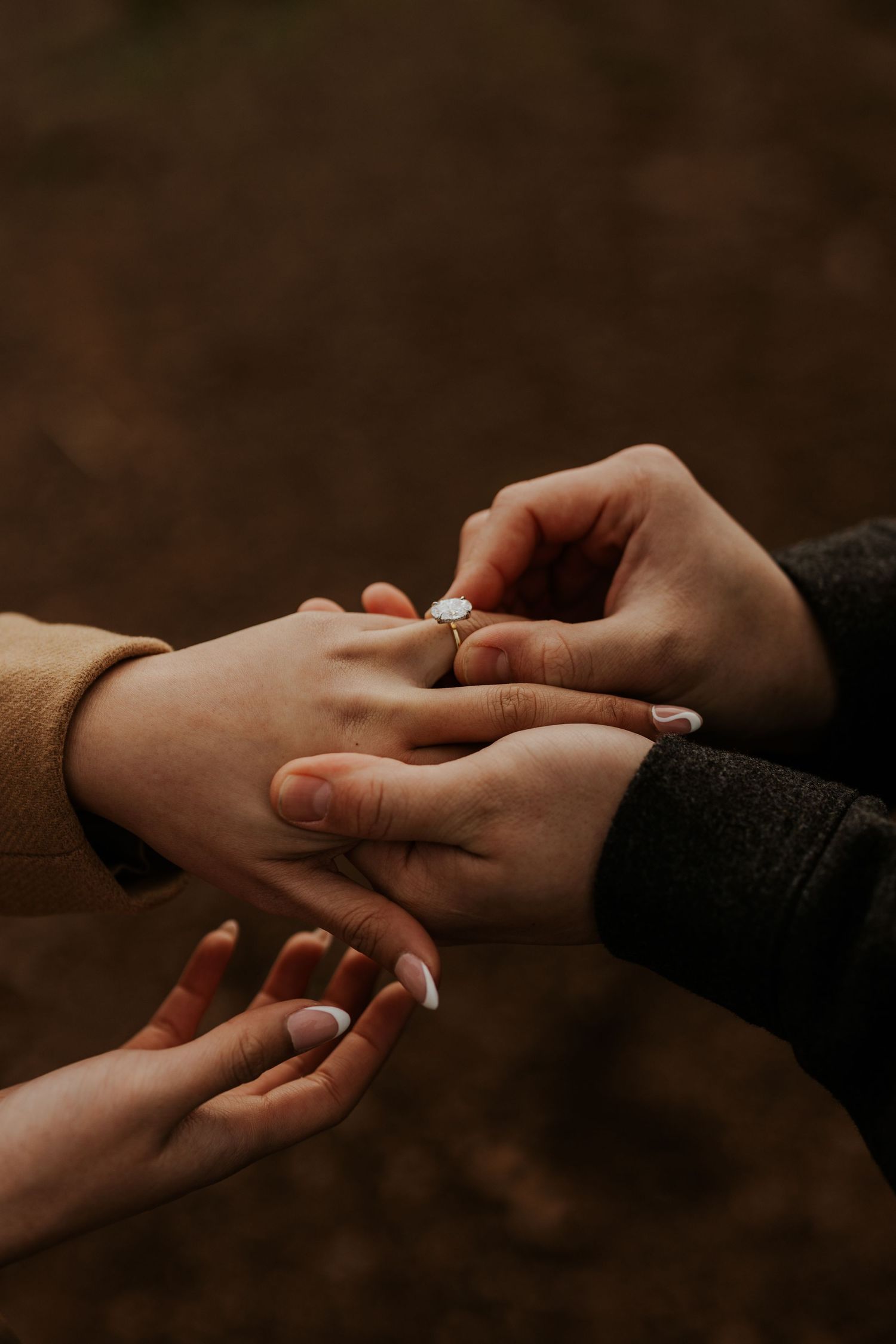 close up of two hands, man putting an engagement ring on woman's hand
