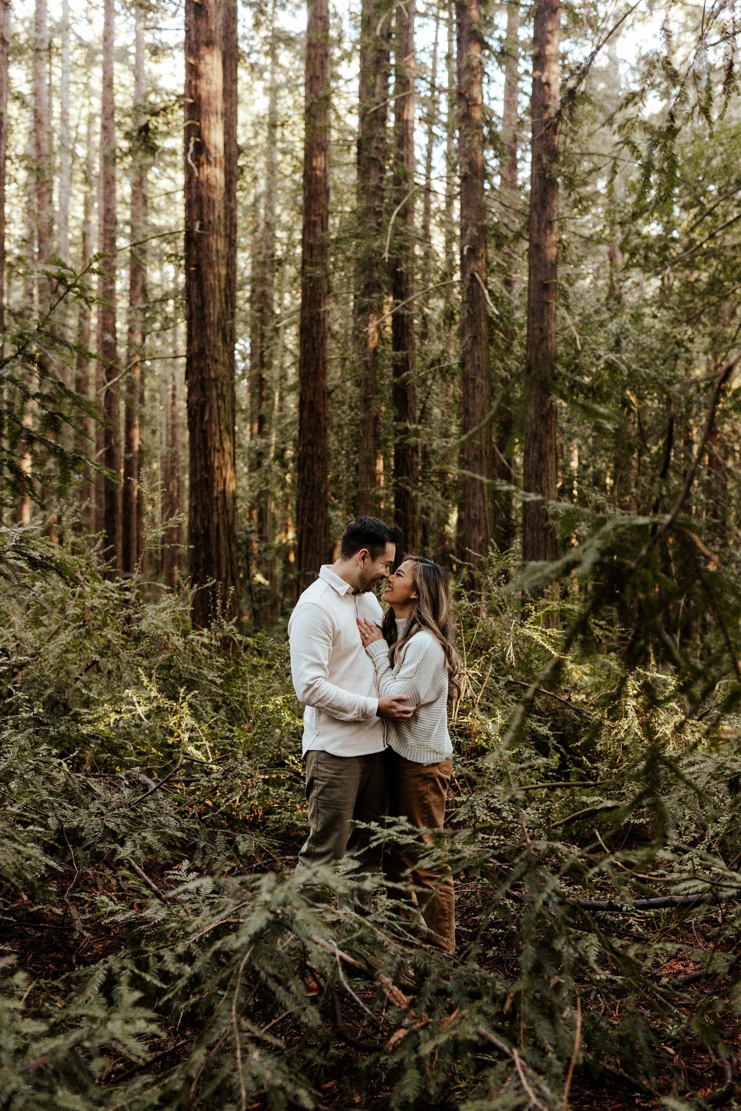 couple in the middle of redwood tress snuggling up, touching noses