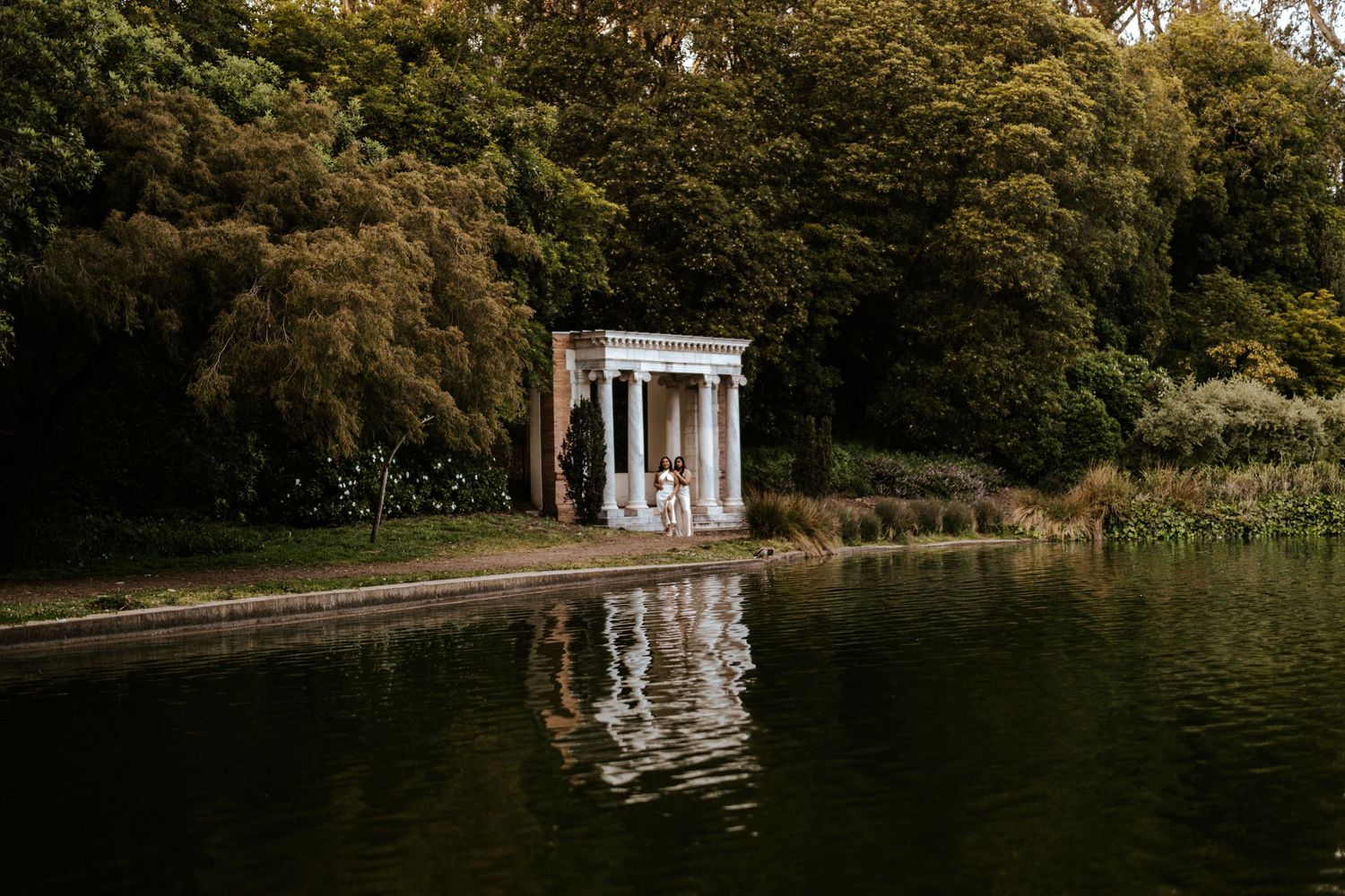 San Francisco Elopement Photographer - couple standing between columns in Golden Gate Park with green lake and trees aro