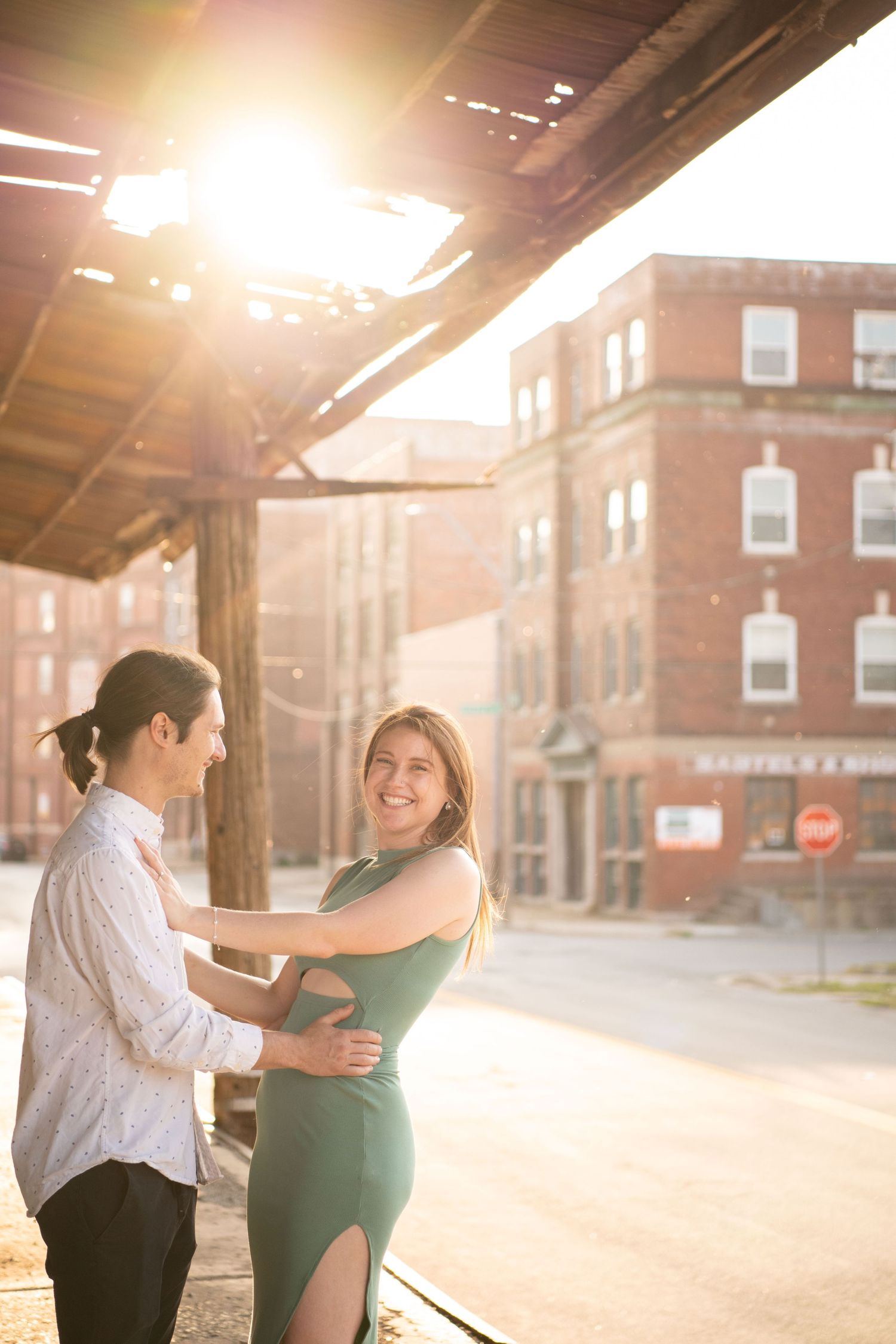 A couple shares a playful embrace under an industrial awning during golden hour.