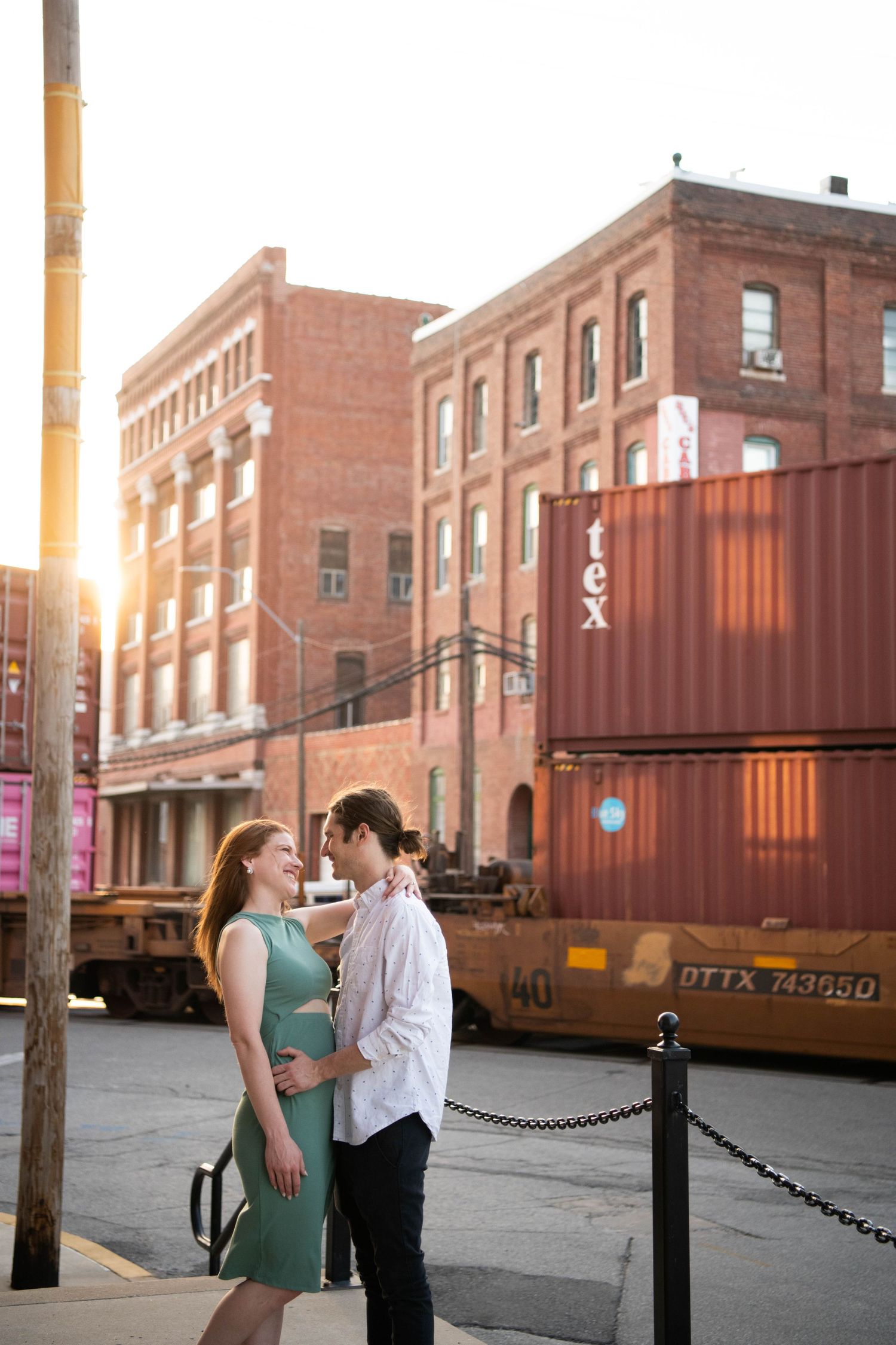 A couple embraces near industrial shipping containers at golden hour.