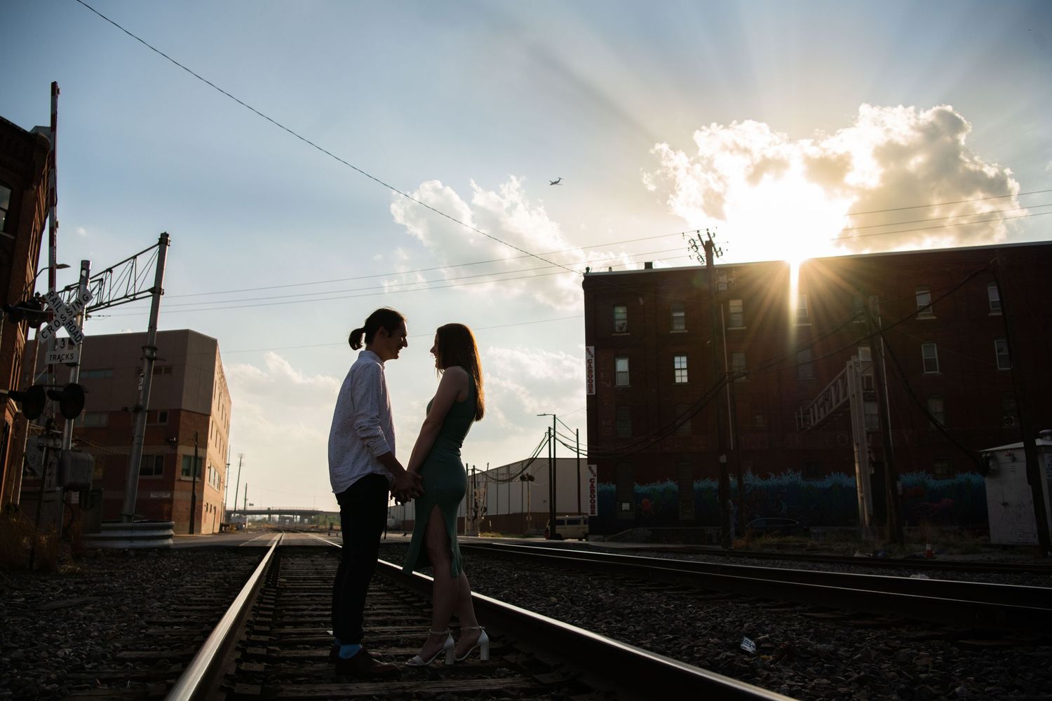 Sunset silhouette of couple standing close together on railroad tracks in urban setting.