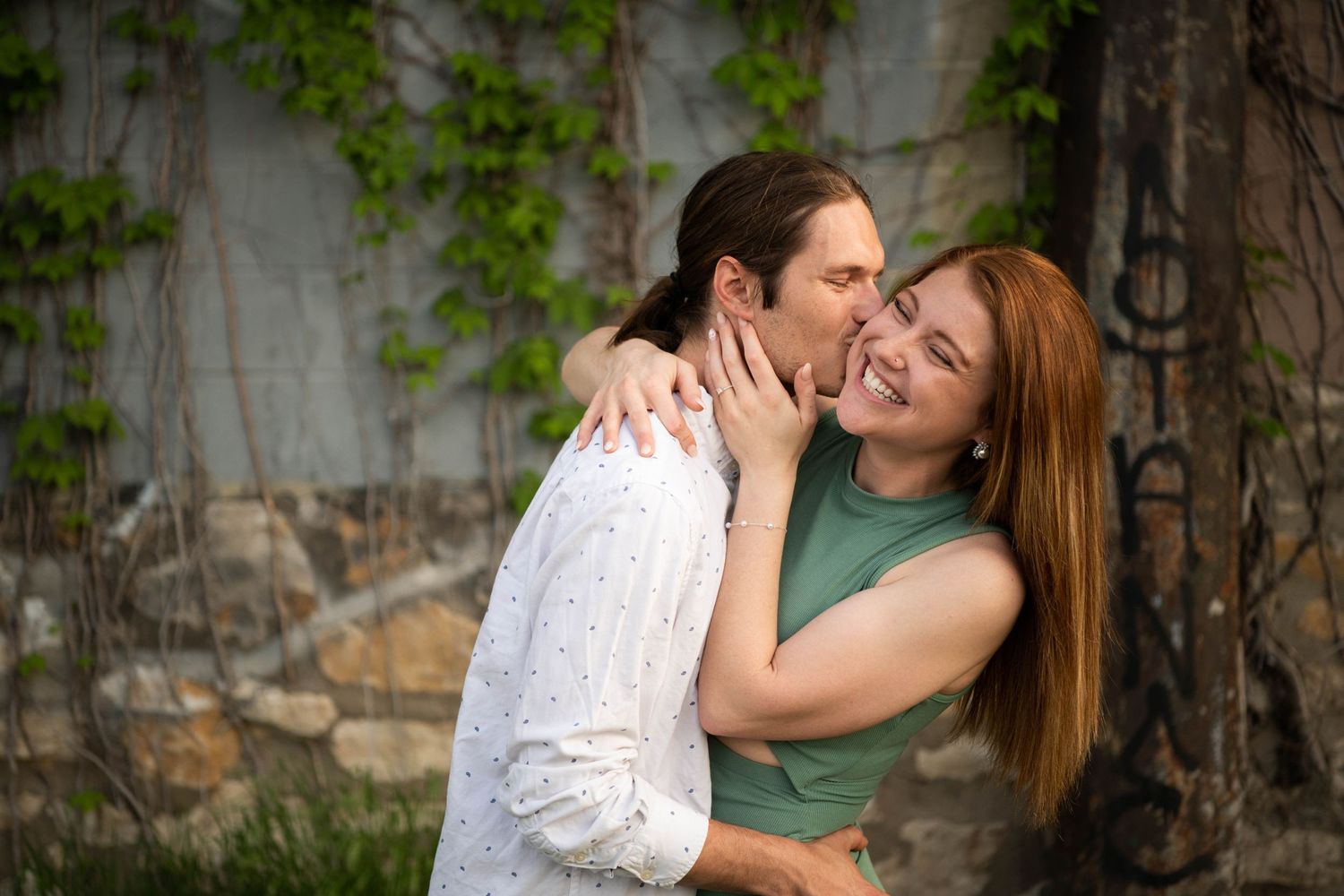 A tender kiss shared between a couple by an ivy-covered wall.
