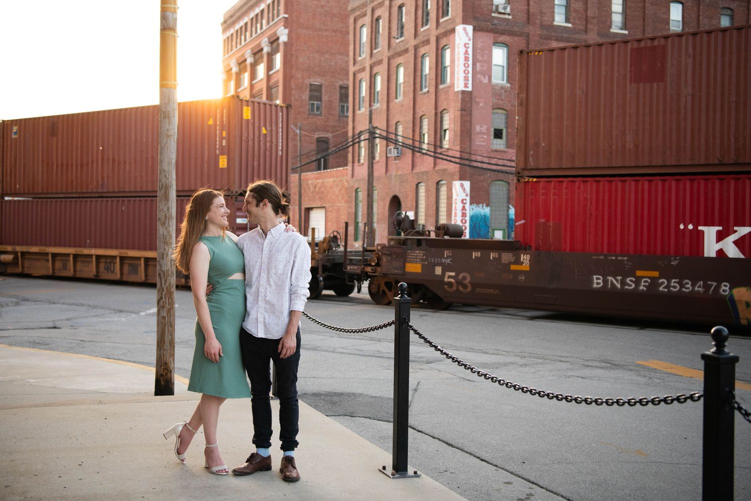 A couple stands near shipping containers at sunset in an industrial district.
