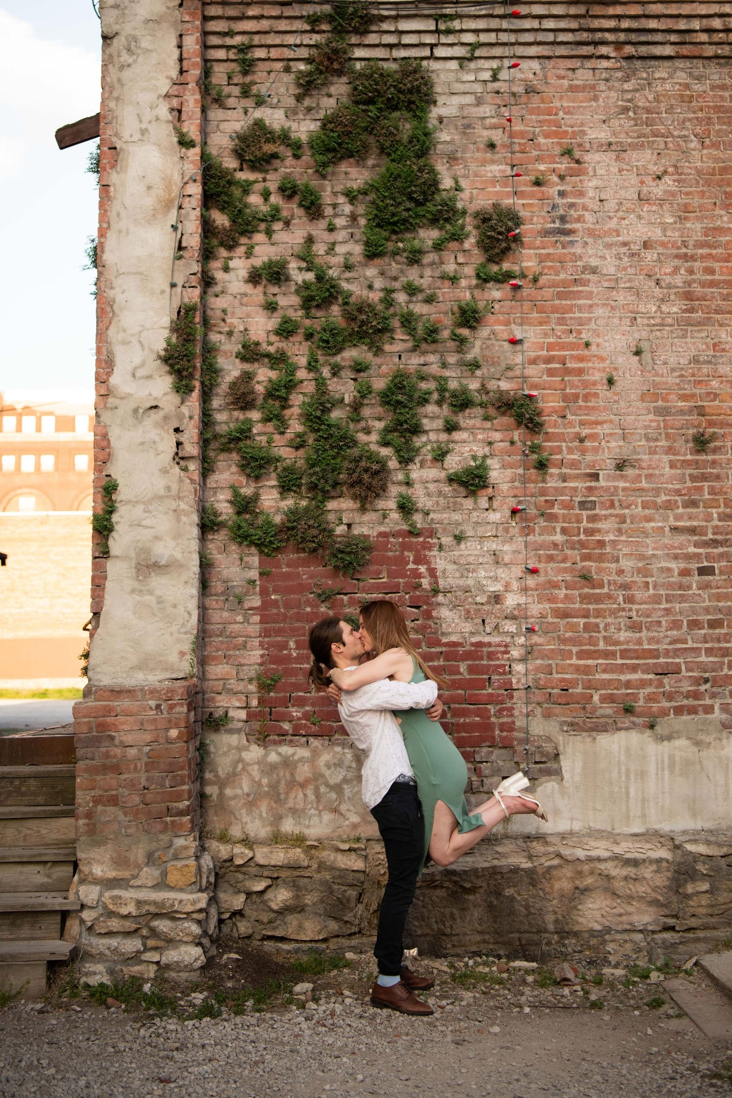 Playful lift pose against ivy-covered brick wall at sunset.