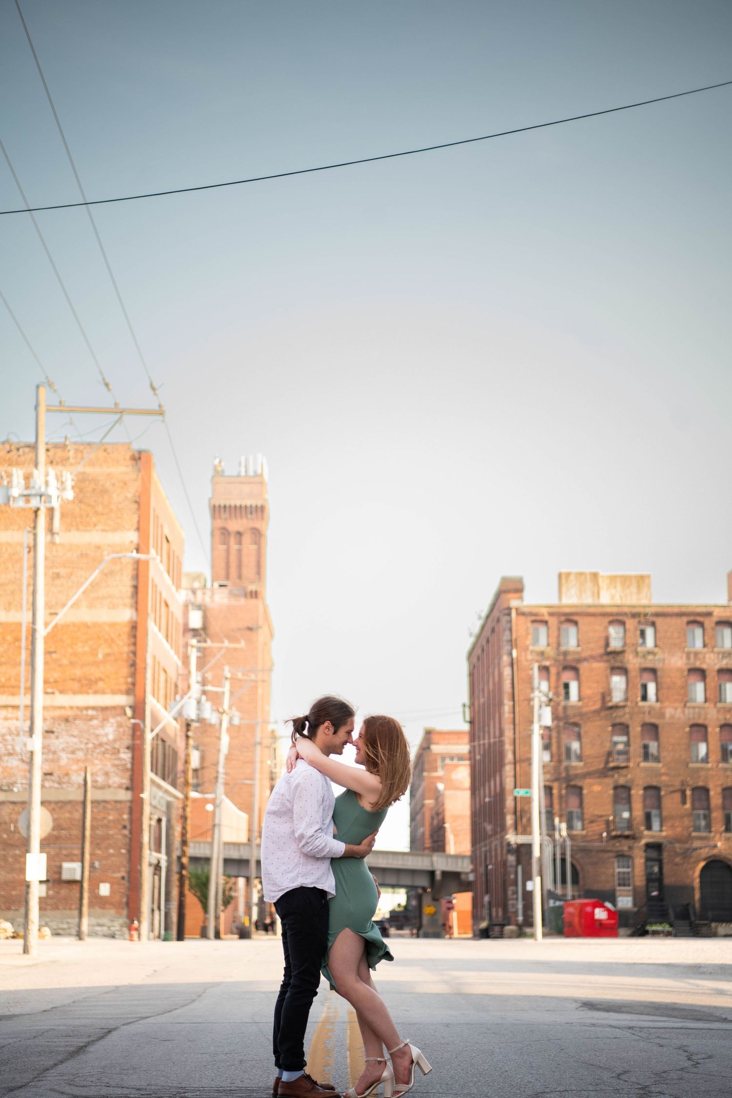 A couple dances in an urban setting with historic brick buildings and power lines in the background.
