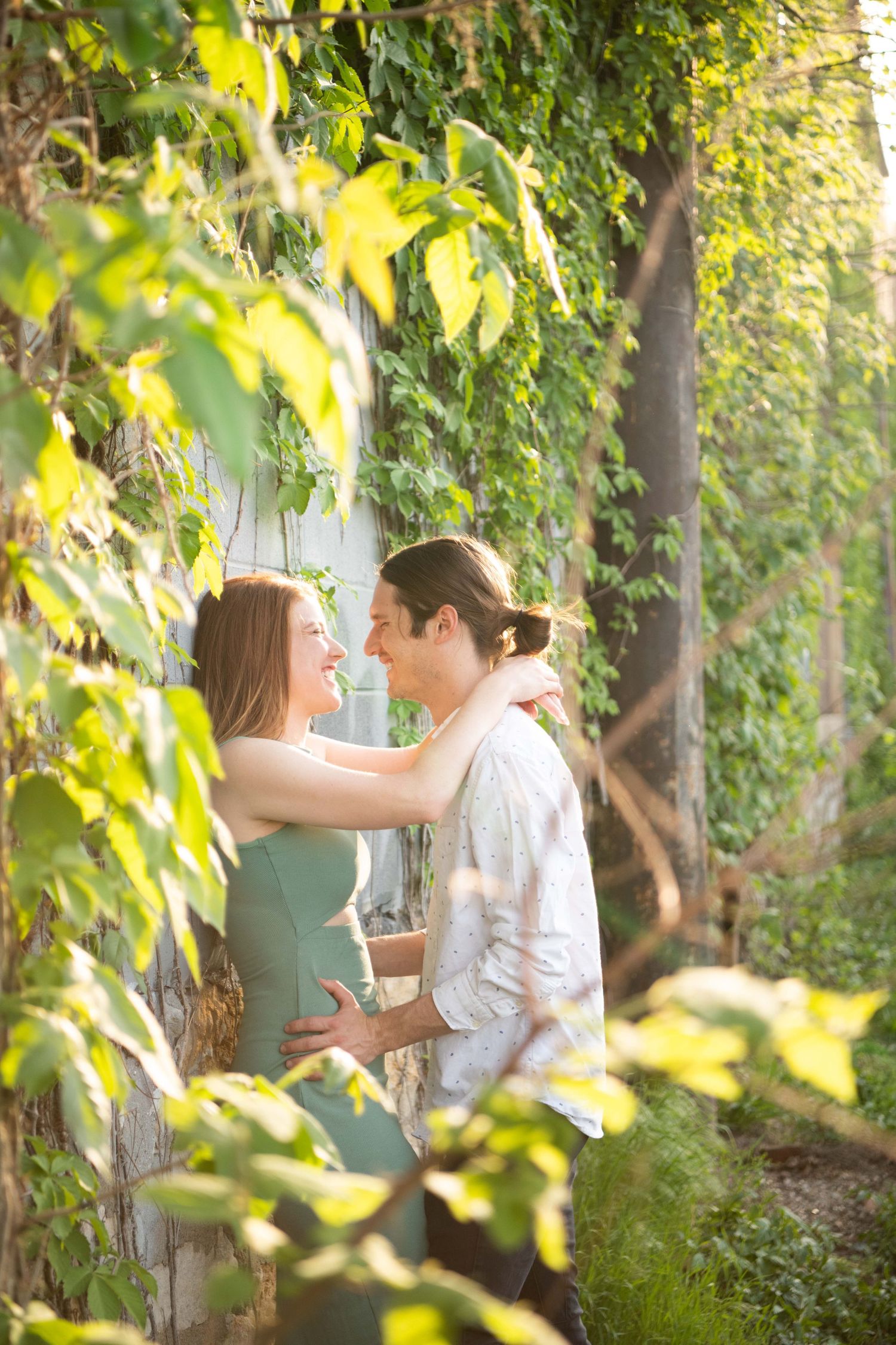 Romantic embrace among green foliage and sunlit leaves.