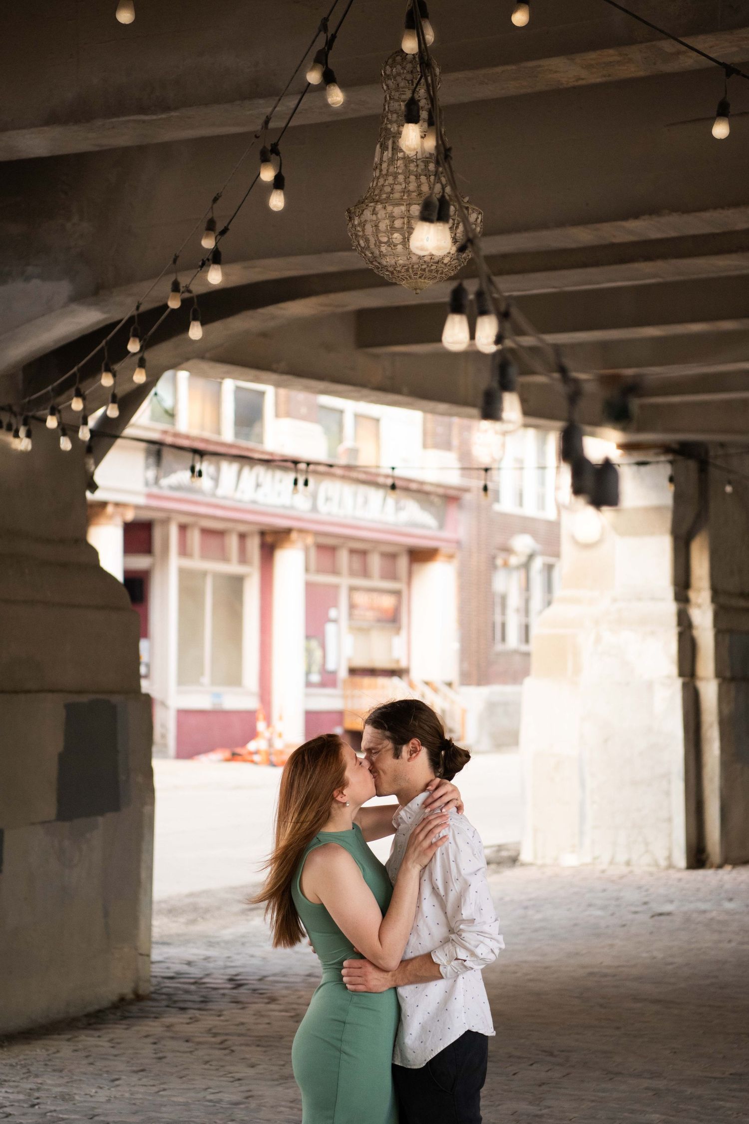 Romantic moment under vintage string lights in urban tunnel setting.