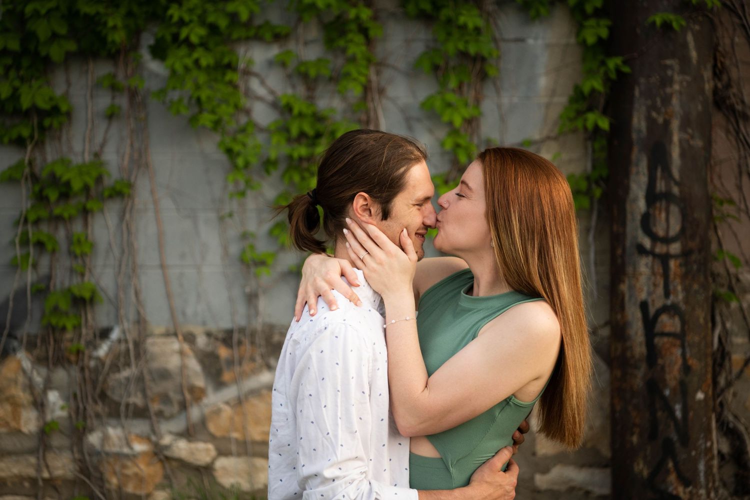 An intimate moment shared between a couple against a vine-covered wall.