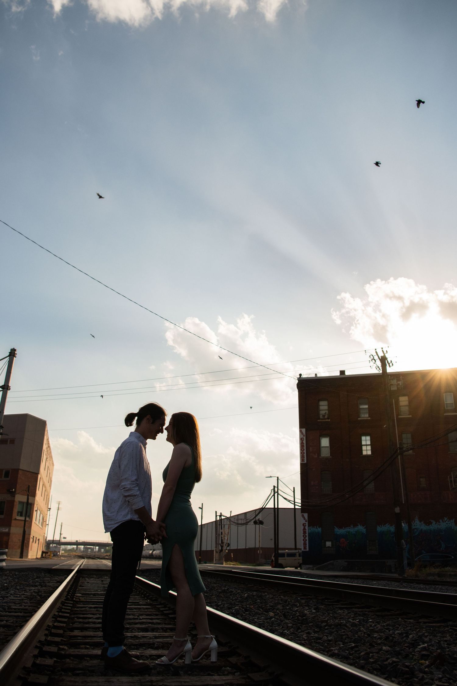 Silhouetted couple on train tracks at sunset with dramatic sky and city buildings.