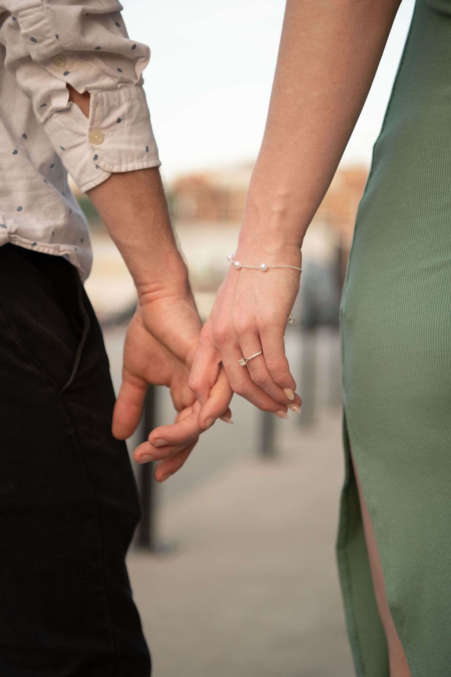 Couple holding hands showing engagement ring and delicate bracelet.