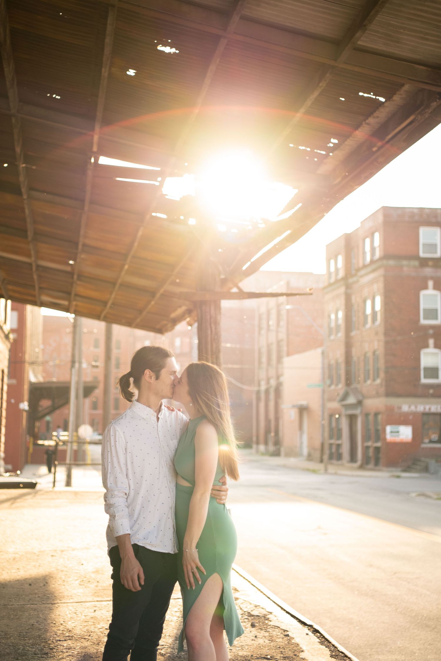 Golden sunlight illuminates a couple sharing an intimate moment under a covered walkway.