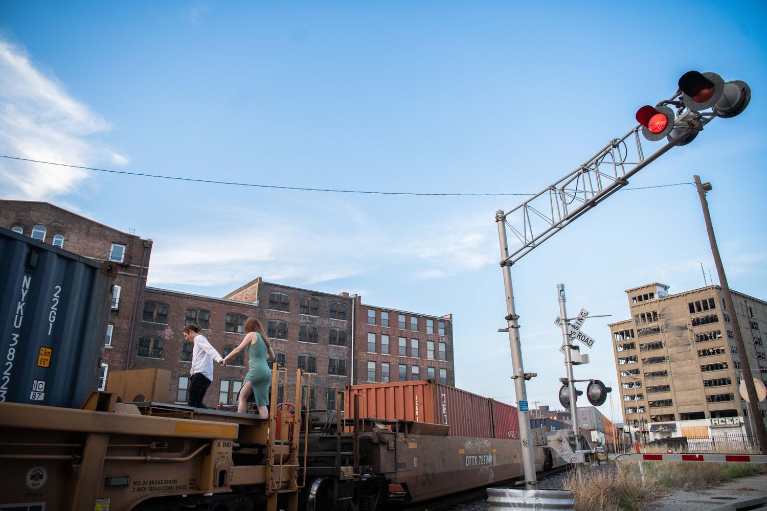 Train car with railroad crossing signal against blue sky and urban landscape.