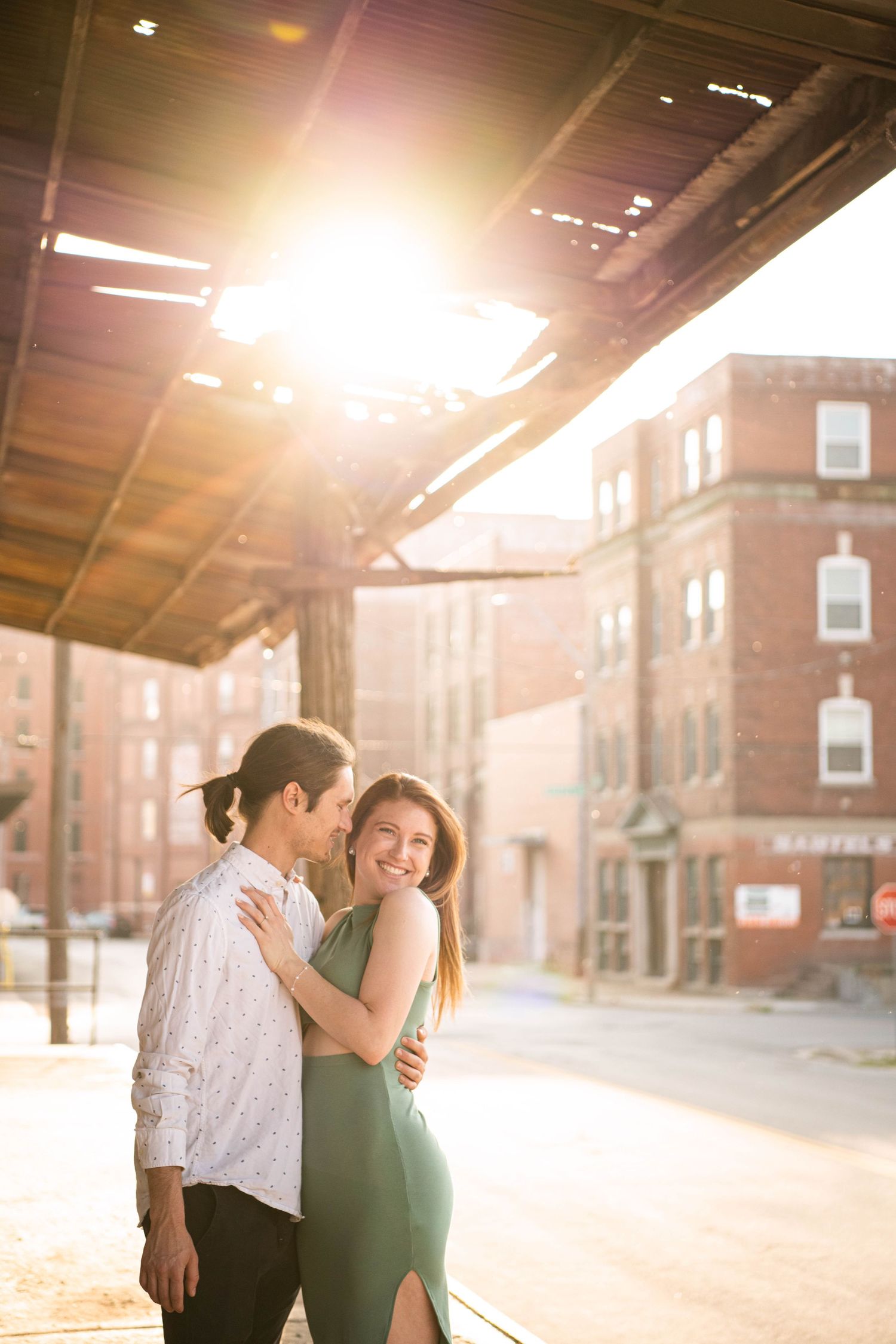 A romantic embrace captured in warm sunlight under an urban industrial overhang.